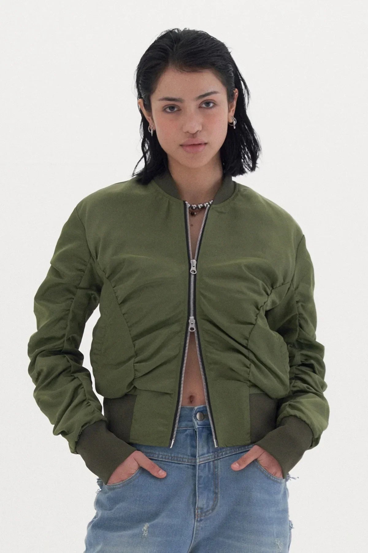 Young woman wearing a khaki ruched bomber jacket with double zipper and blue jeans