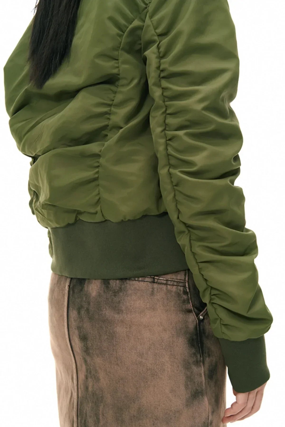 Close-up of a person wearing a ruched khaki green jacket with elastic cuffs and a faded brown skirt