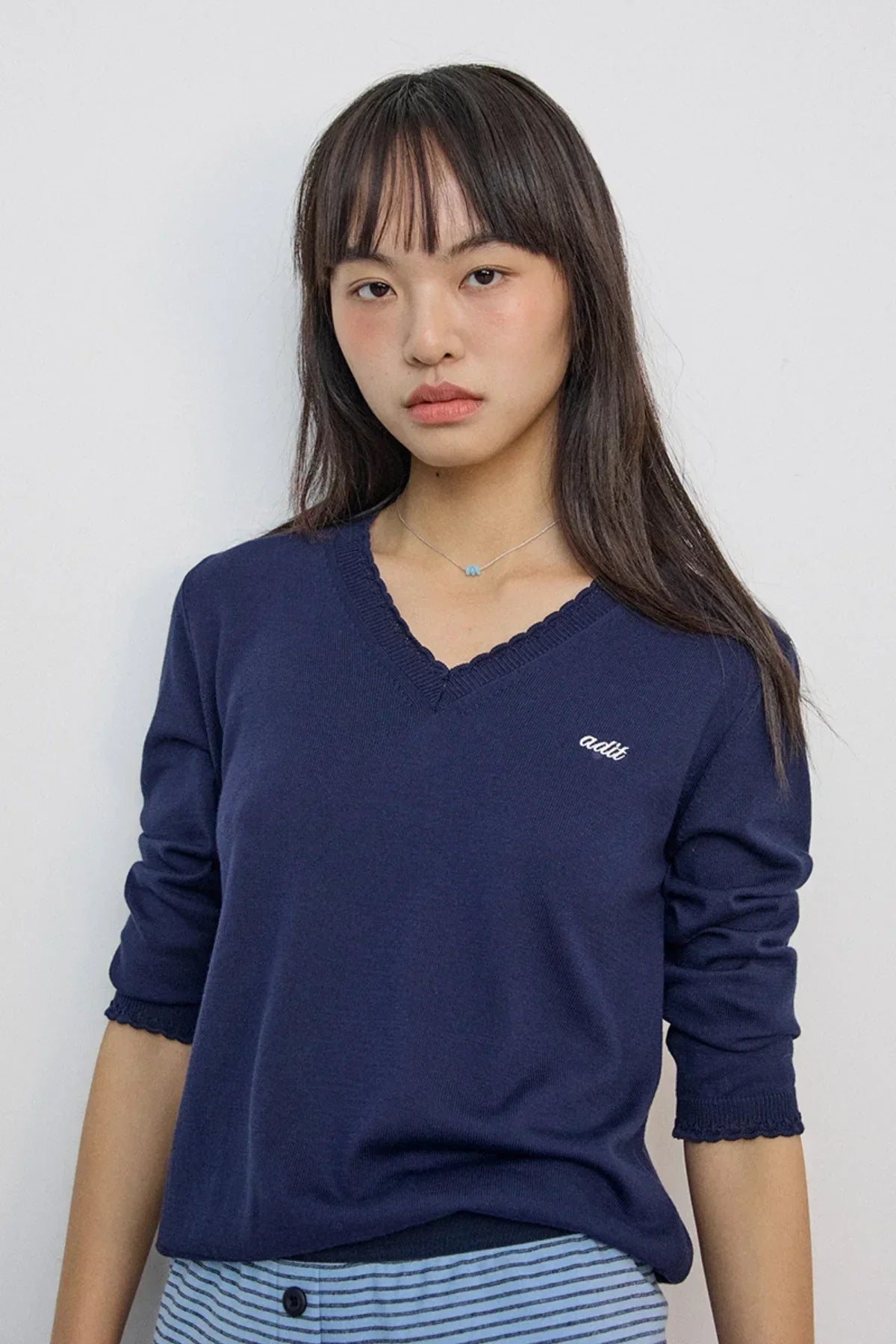 Woman wearing small blue bead necklace with navy blue V-neck sweater and striped pants