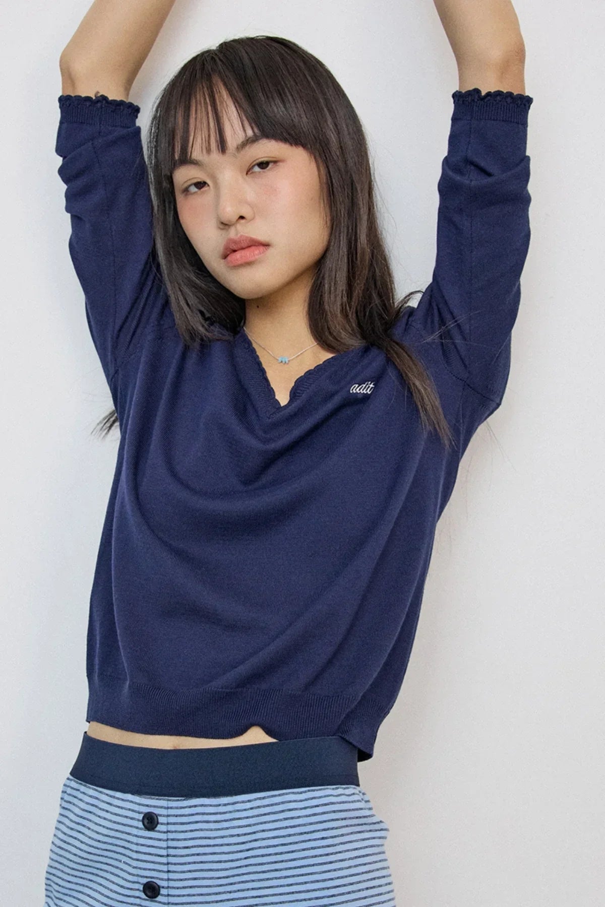 Young woman wearing navy blue sweater and striped pants posing with arms raised against white background