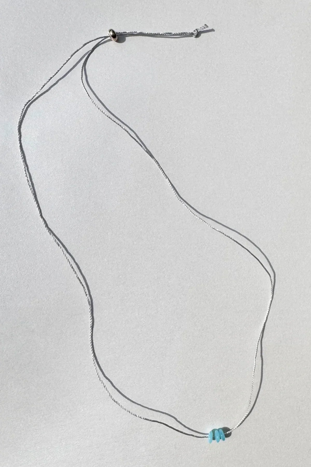 Delicate silver necklace with three small blue beads on a plain light background