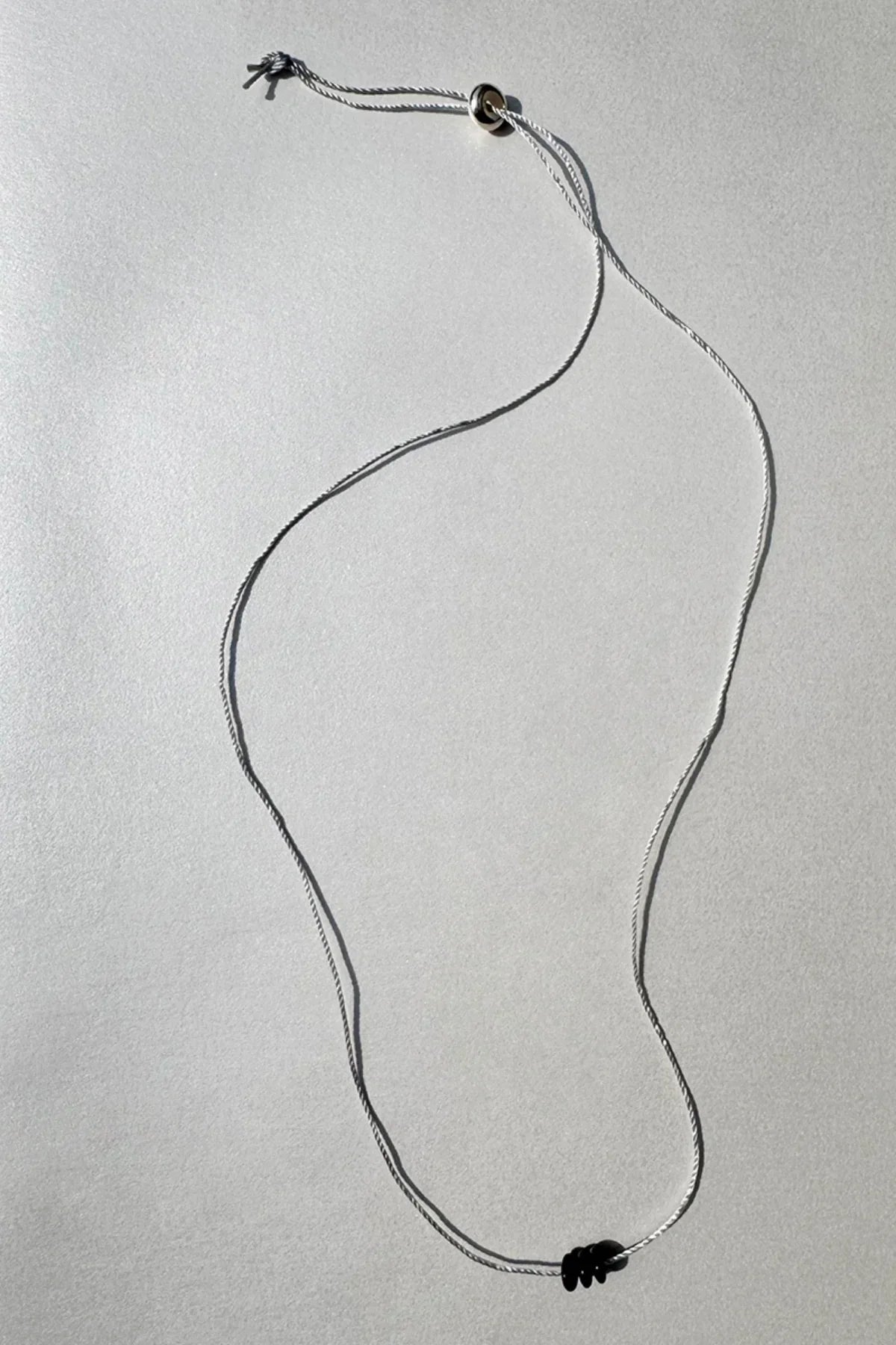Minimalistic white cord necklace with three small black beads on a light gray background