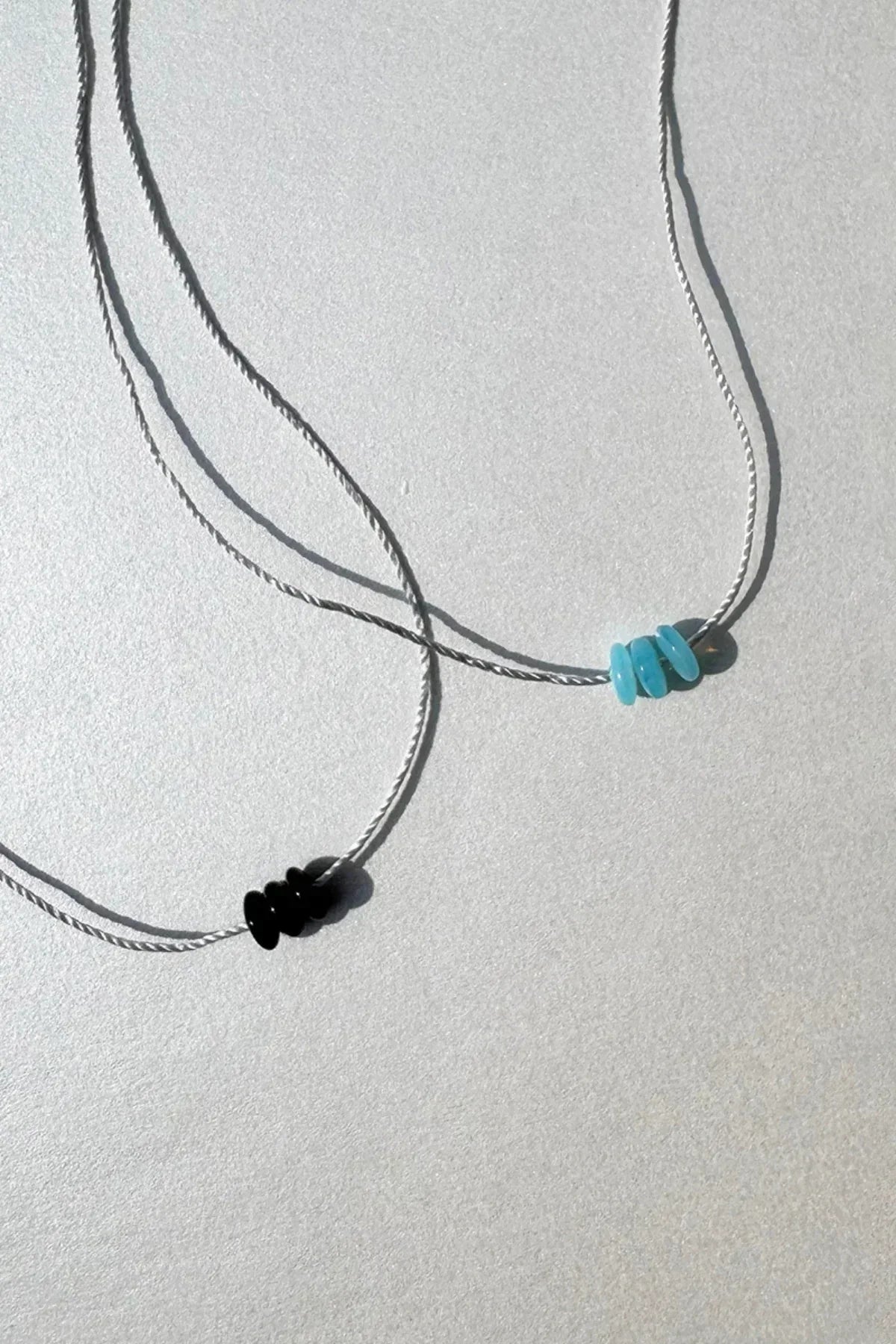 Close-up of two minimalist necklaces with small black and turquoise beads on thin cords