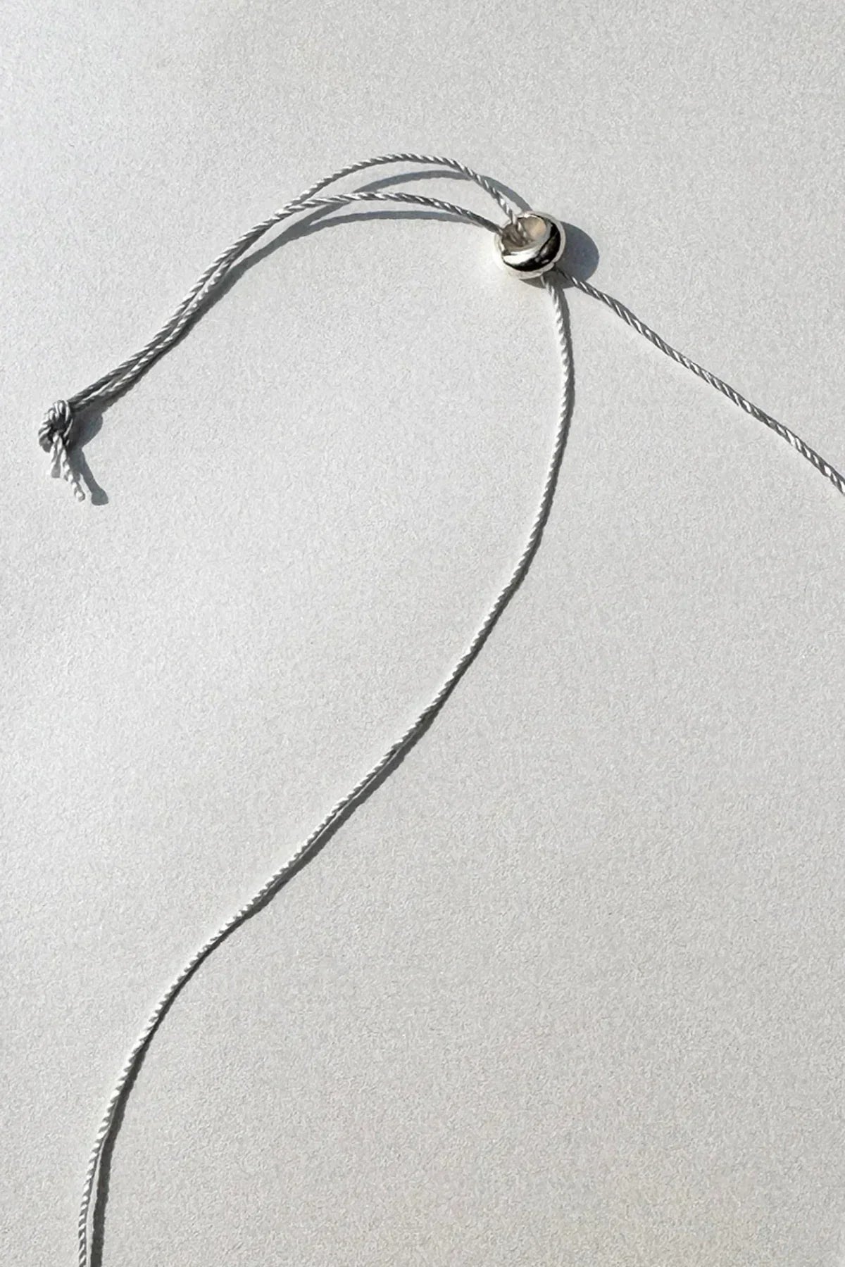 Close-up of a silver sliding bead clasp on a white twisted cord necklace against a light background