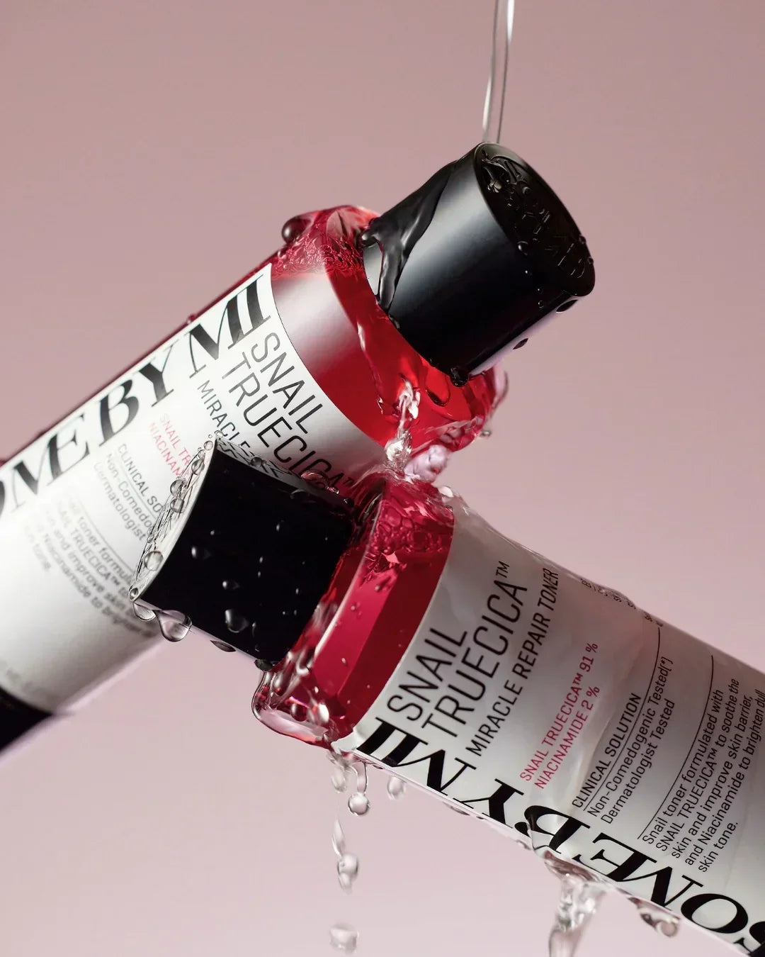 Two Son&BriHM Snail Truecica Miracle Repair skincare bottles with water splashing on light pink background