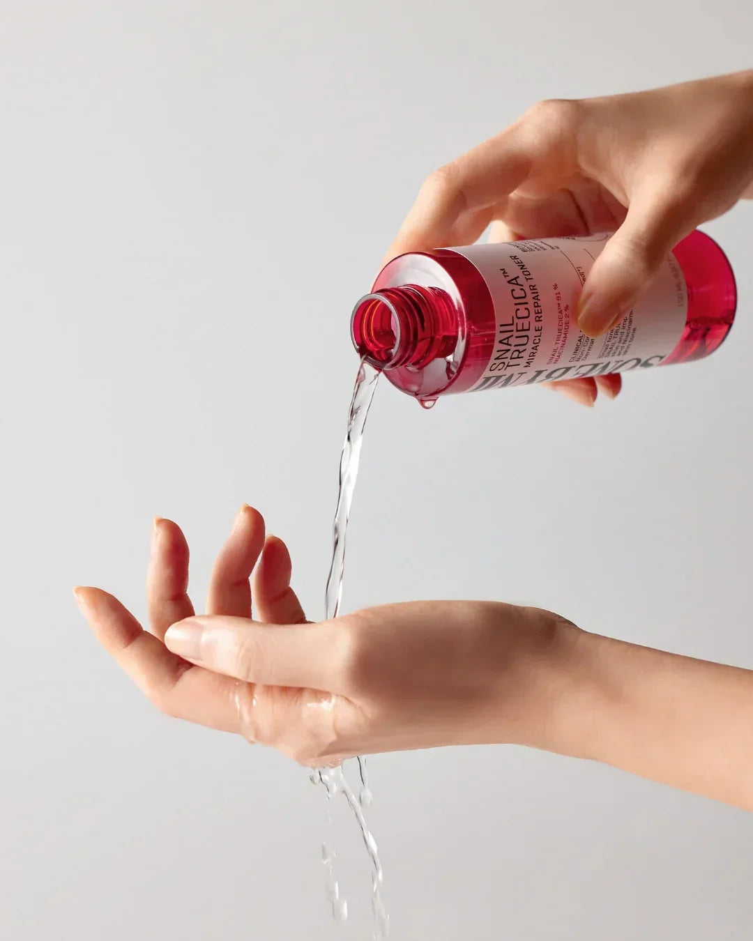 Hand pouring Snail Truecica Miracle Repair Toner from pink bottle onto open palm against white background