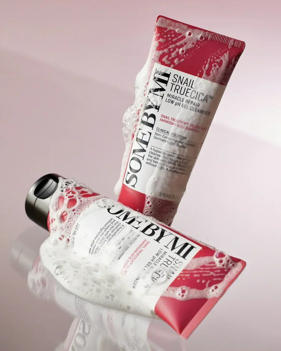 SOME BY MI Snail Truecica Miracle Repair Low PH Gel Cleanser tubes covered in foam on pink reflective surface
