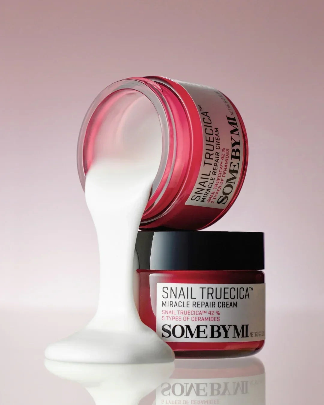 SOME BY MI Snail Truecica Miracle Repair Cream jars with cream flowing from one jar on a pink background