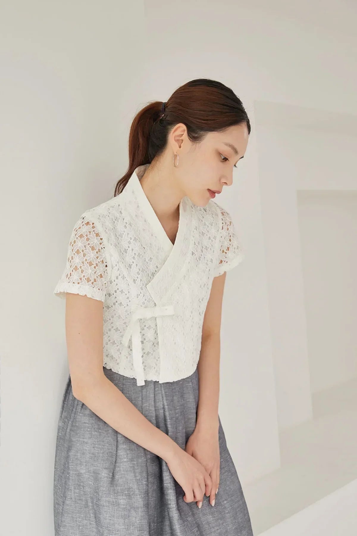 Woman wearing white lace short-sleeve jeogori with grey skirt in minimal white room