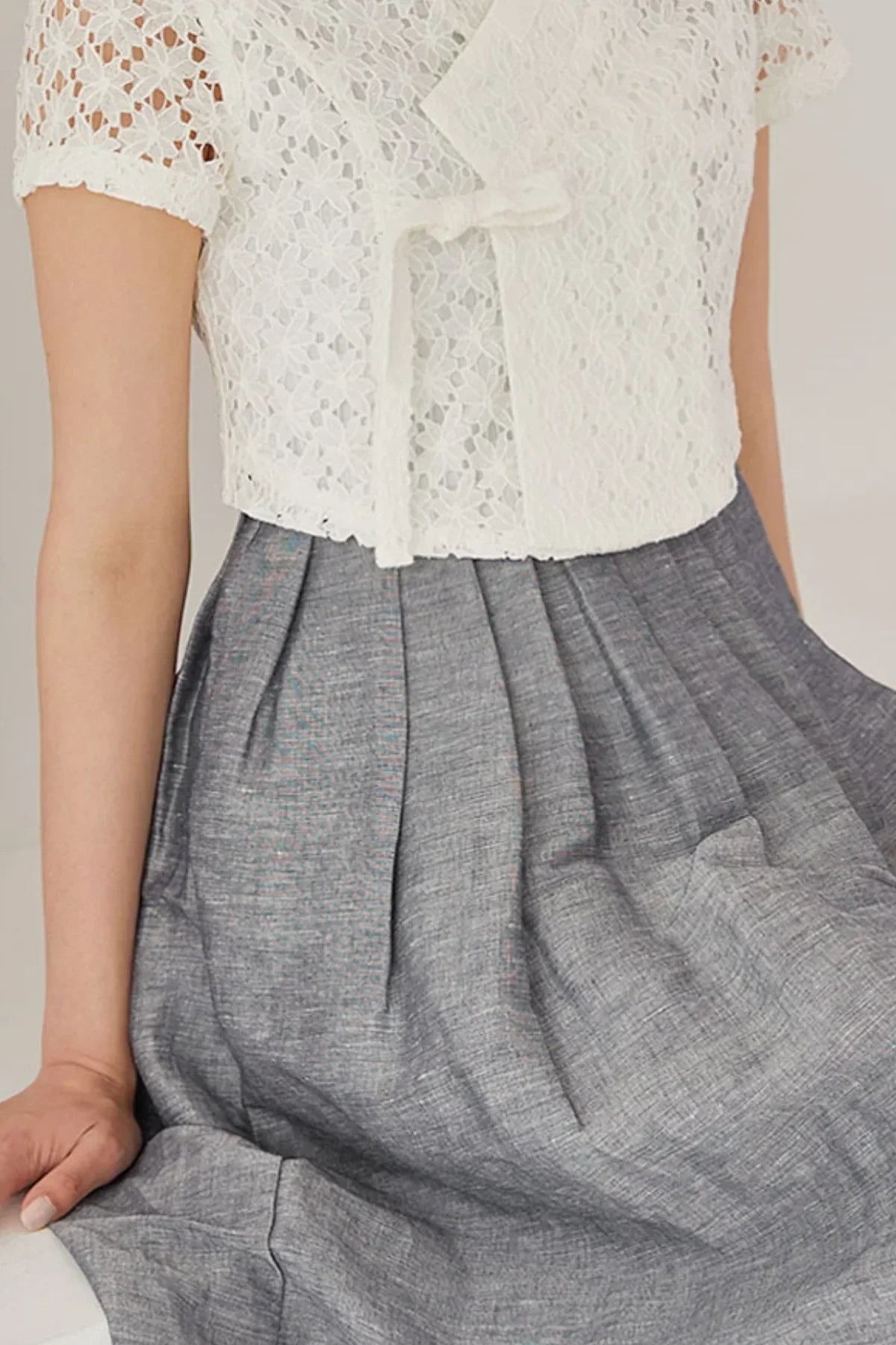 White floral lace short sleeve blouse with a knot tie, paired with a high-waisted pleated grey skirt