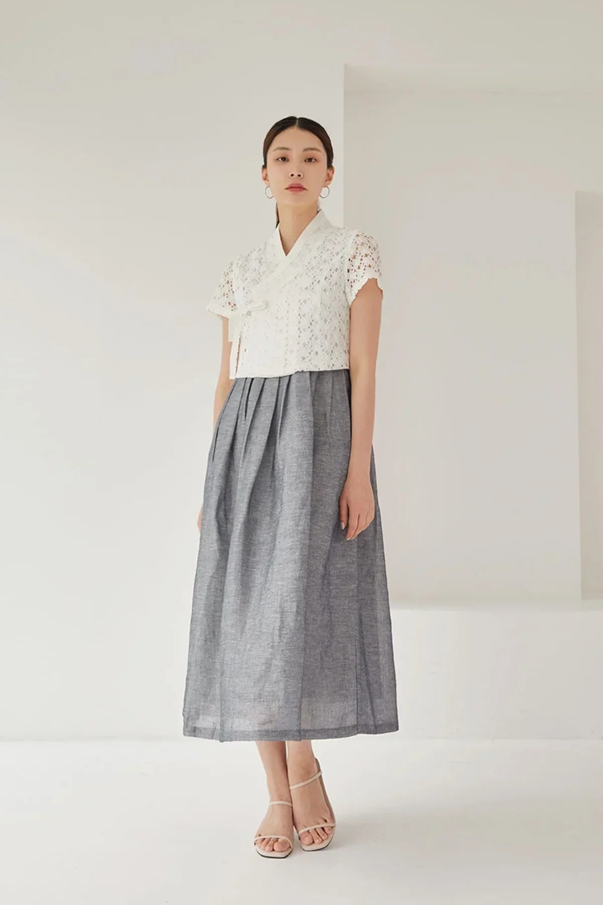 Woman wearing a white lace short-sleeve jeogori and gray pleated hanbok skirt in minimal studio