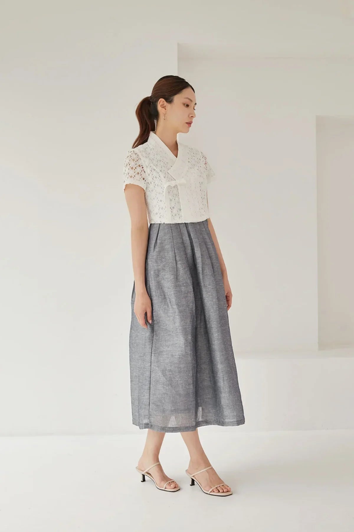 Woman wearing white lace short-sleeve jeogori and gray midi skirt with beige heeled sandals