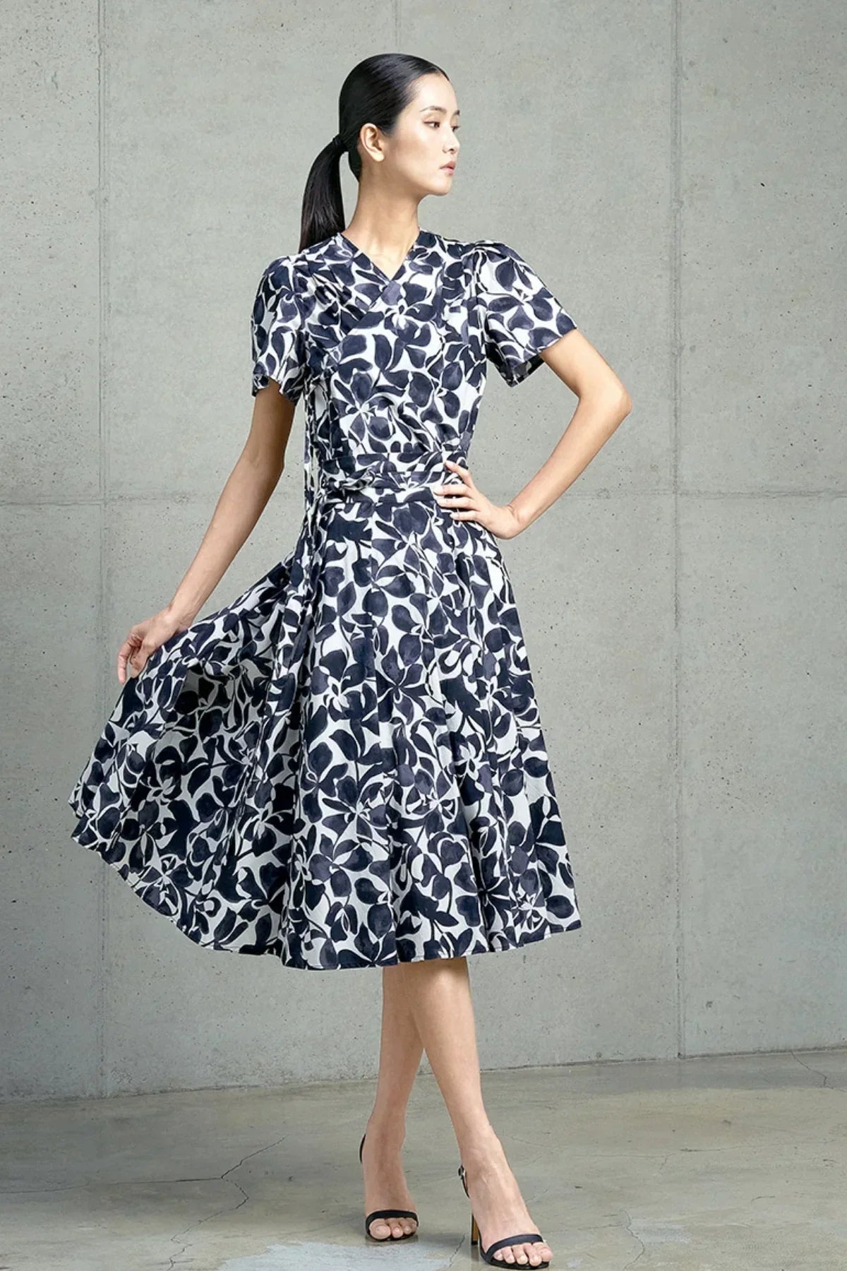 Woman in navy leaf-print wrap dress with short sleeves posing indoors against concrete wall