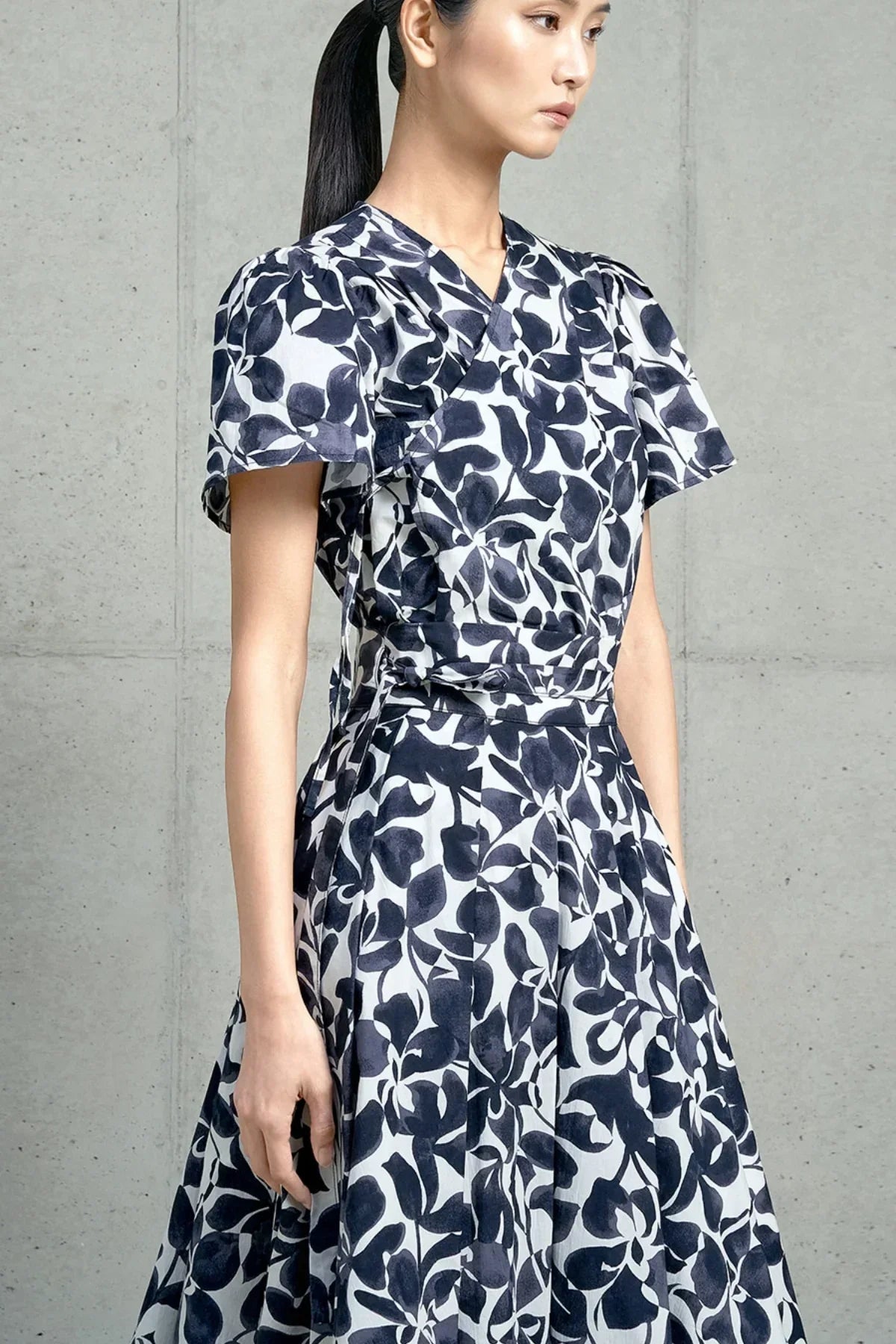 Woman wearing a navy and white floral wrap dress with short sleeves against a concrete wall