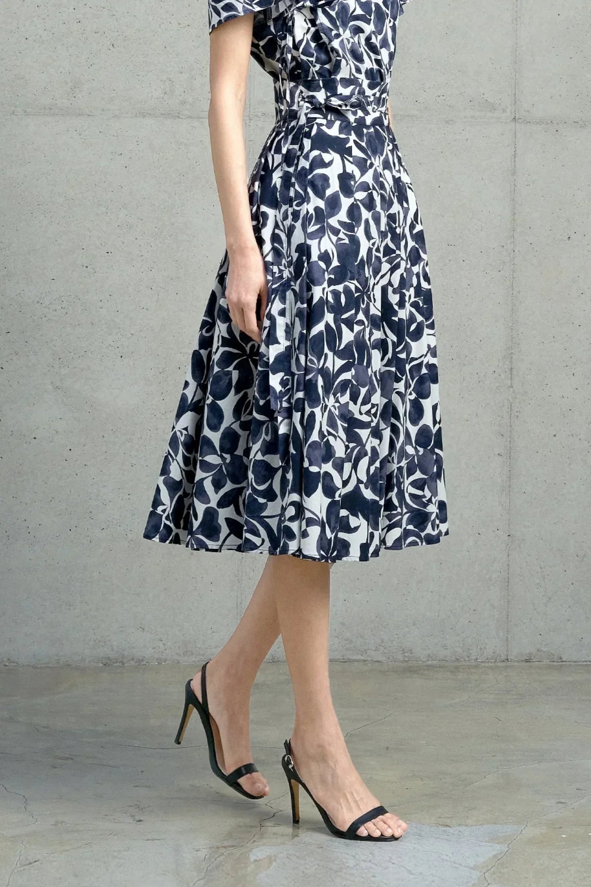 Woman wearing navy floral midi skirt paired with black high heel sandals against concrete wall