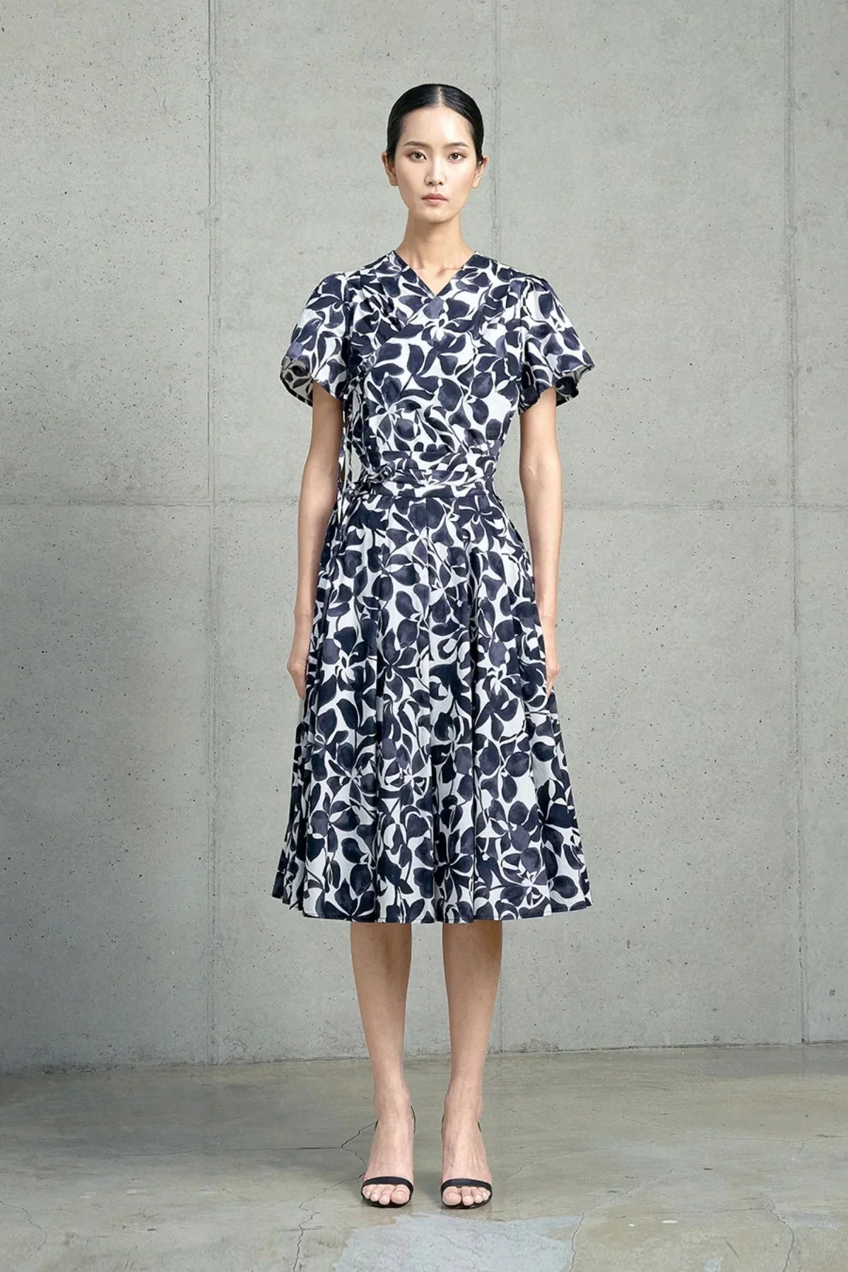 Woman wearing a navy and white floral wrap dress with puff sleeves standing against a concrete wall