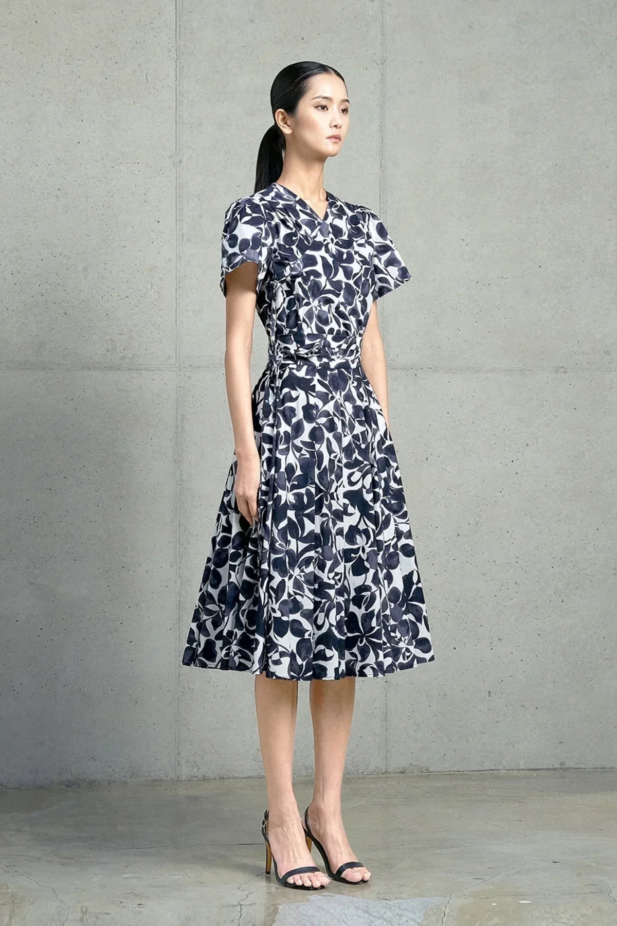 Woman wearing navy and white floral midi dress and black high heel sandals against gray concrete wall