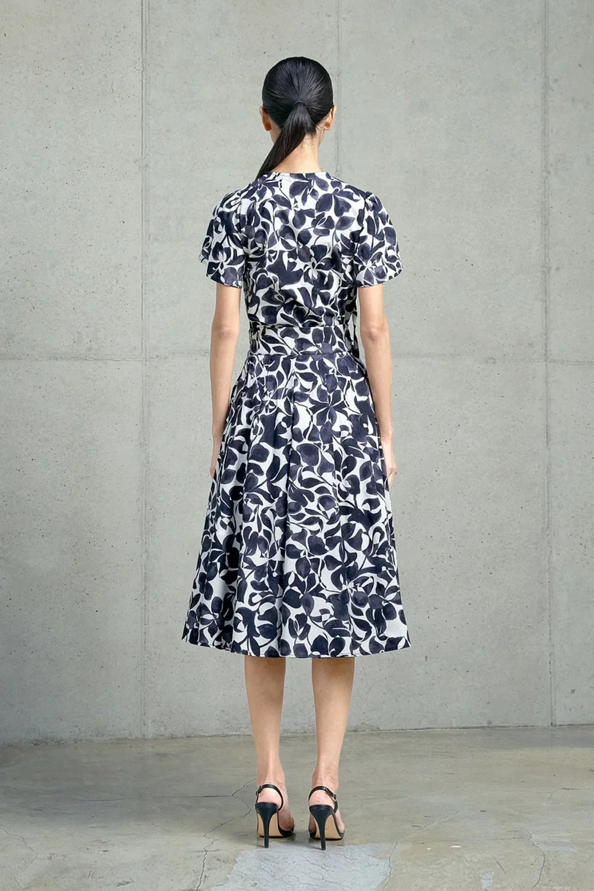 Rear view of woman wearing navy and white floral midi skirt and matching top with short sleeves, black heels