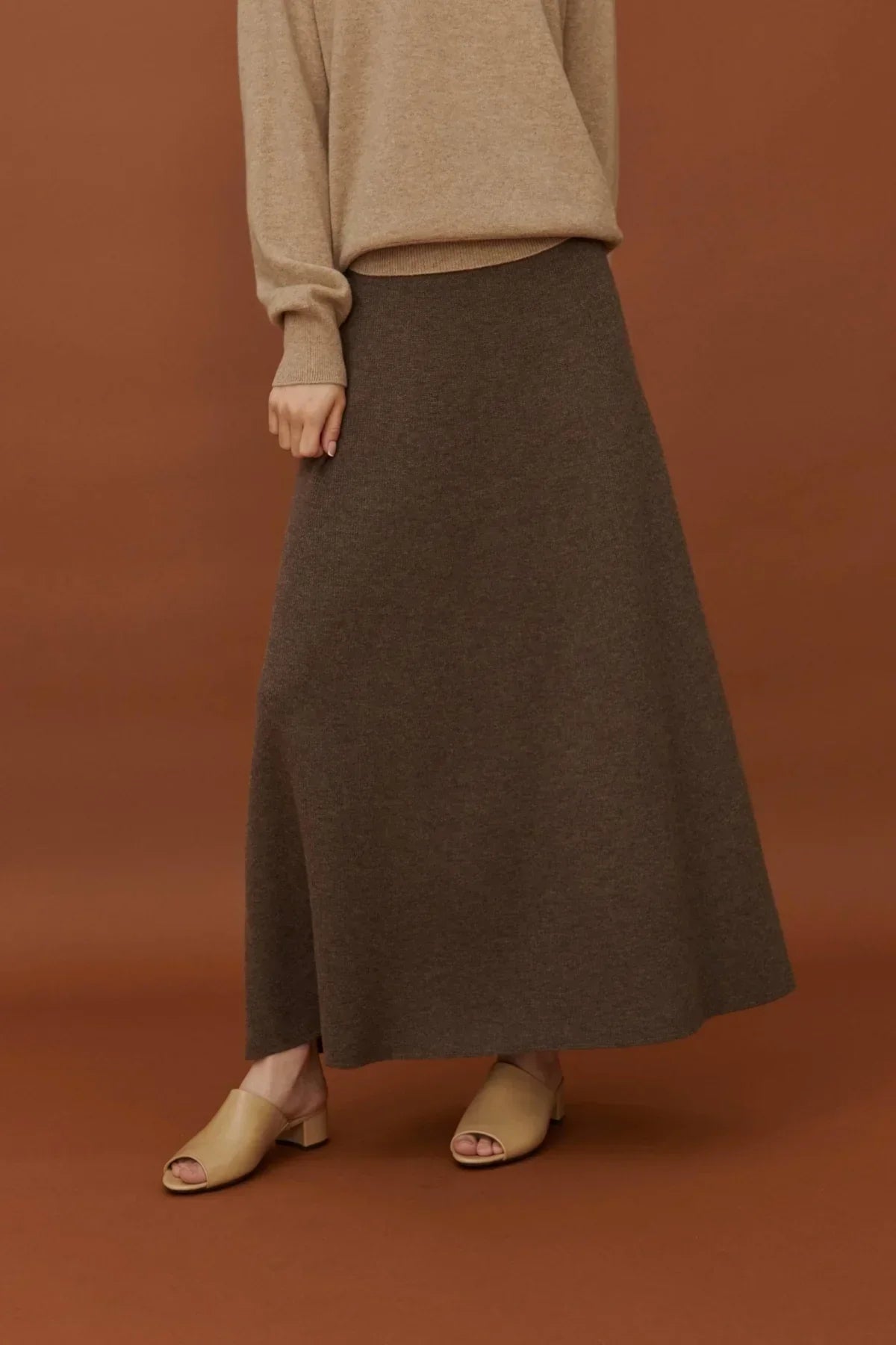 Woman wearing a brown soft A-line knit skirt with beige sweater and beige open-toe block heel shoes