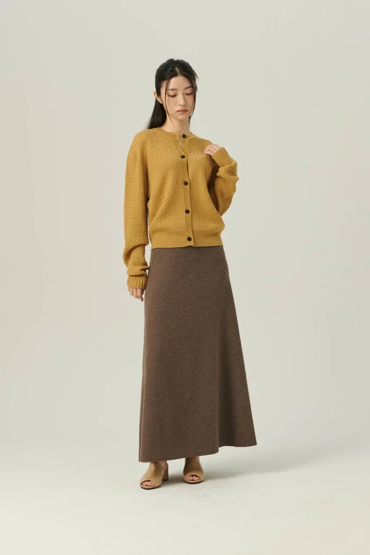 Woman wearing mustard yellow knit cardigan and brown soft A-line knit skirt with beige sandals