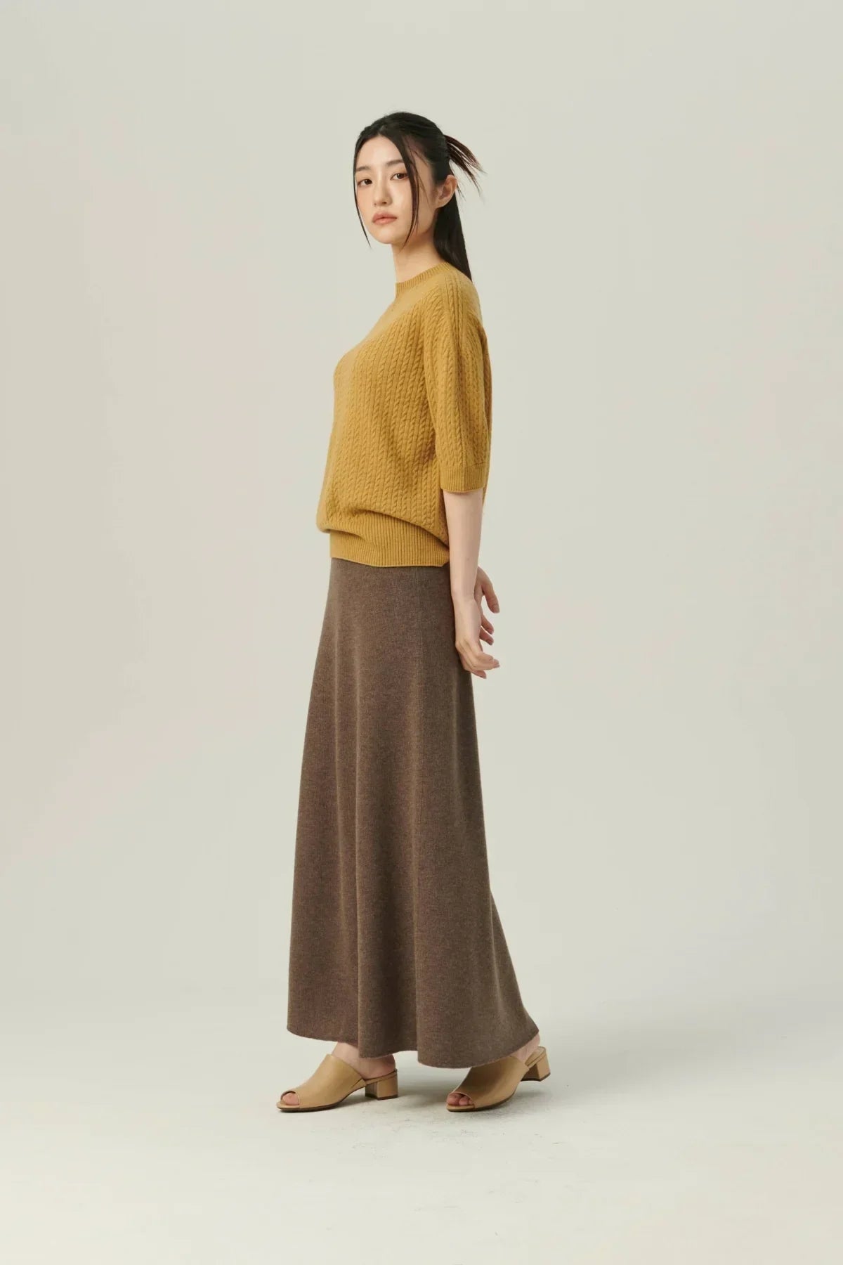 Model wearing mustard knit top and brown soft A-line knit skirt with beige open-toe block heels