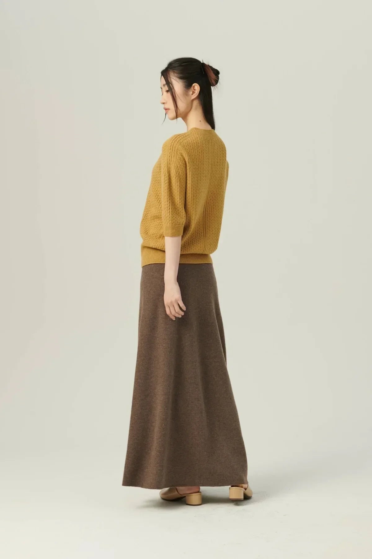 Woman wearing a mustard knit sweater and long brown soft A-line knit skirt with beige shoes