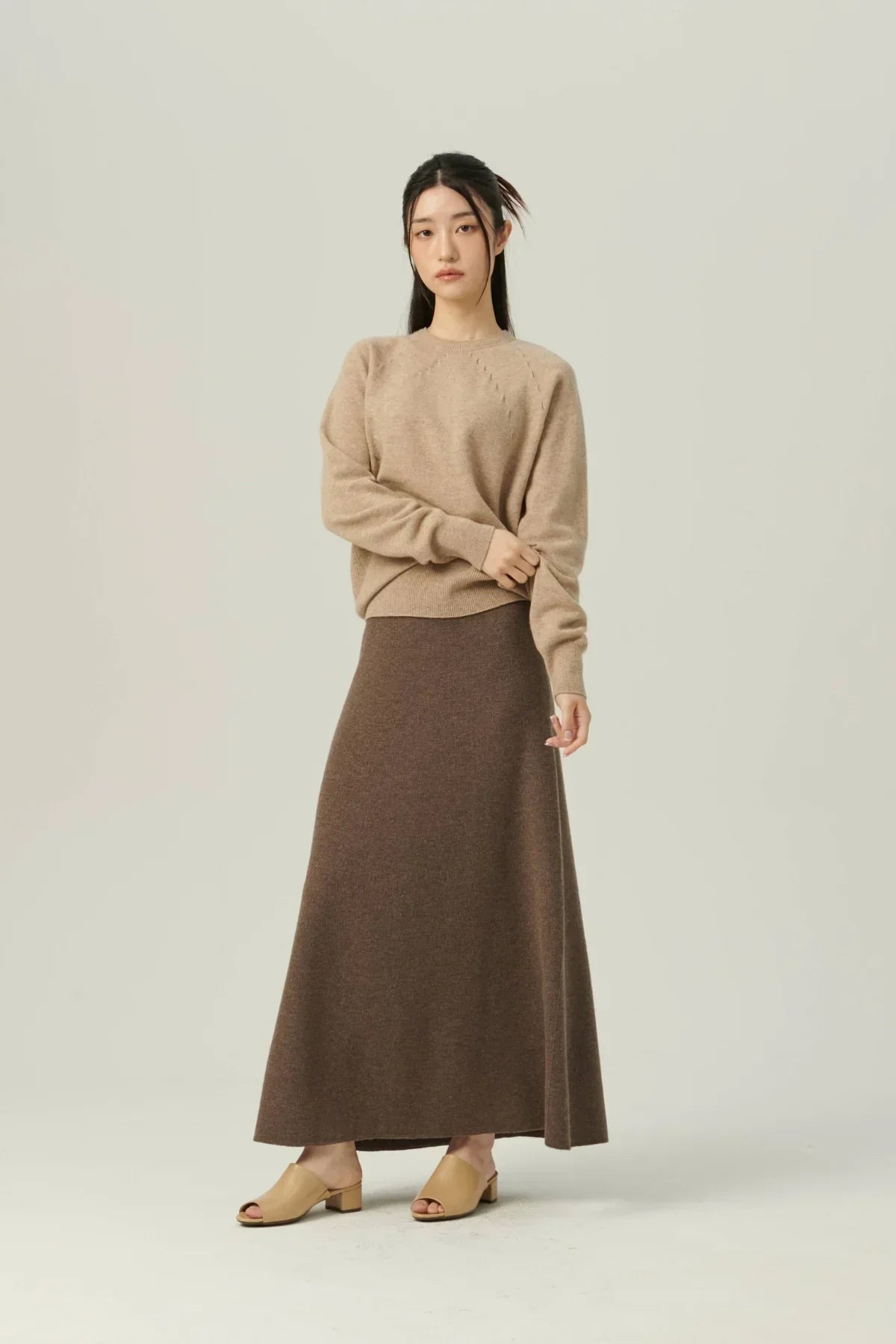 Woman in beige sweater and brown A-line knit skirt with beige block heel sandals on light background