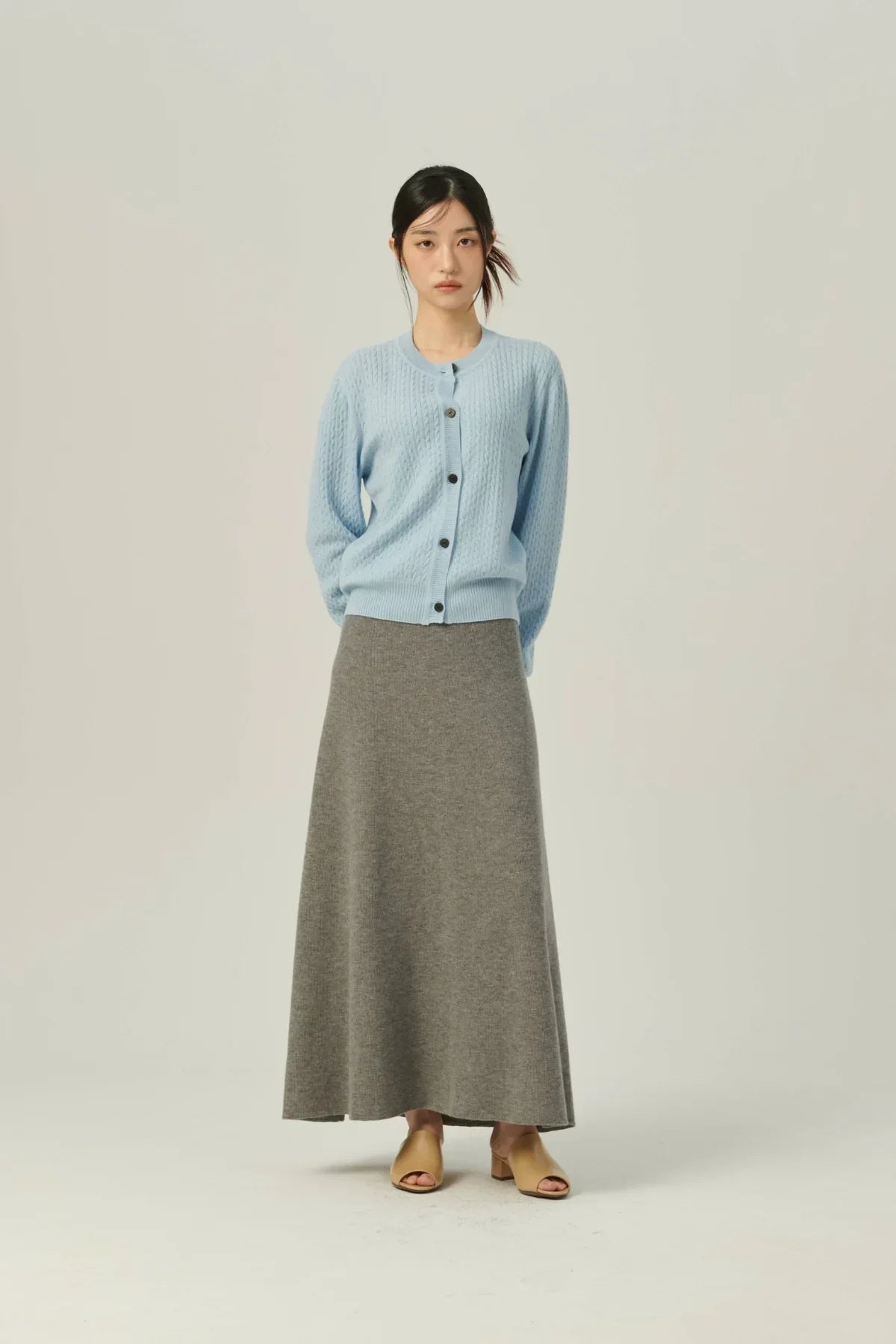 Woman wearing light blue knit cardigan and gray A-line knit skirt with beige open-toe heels