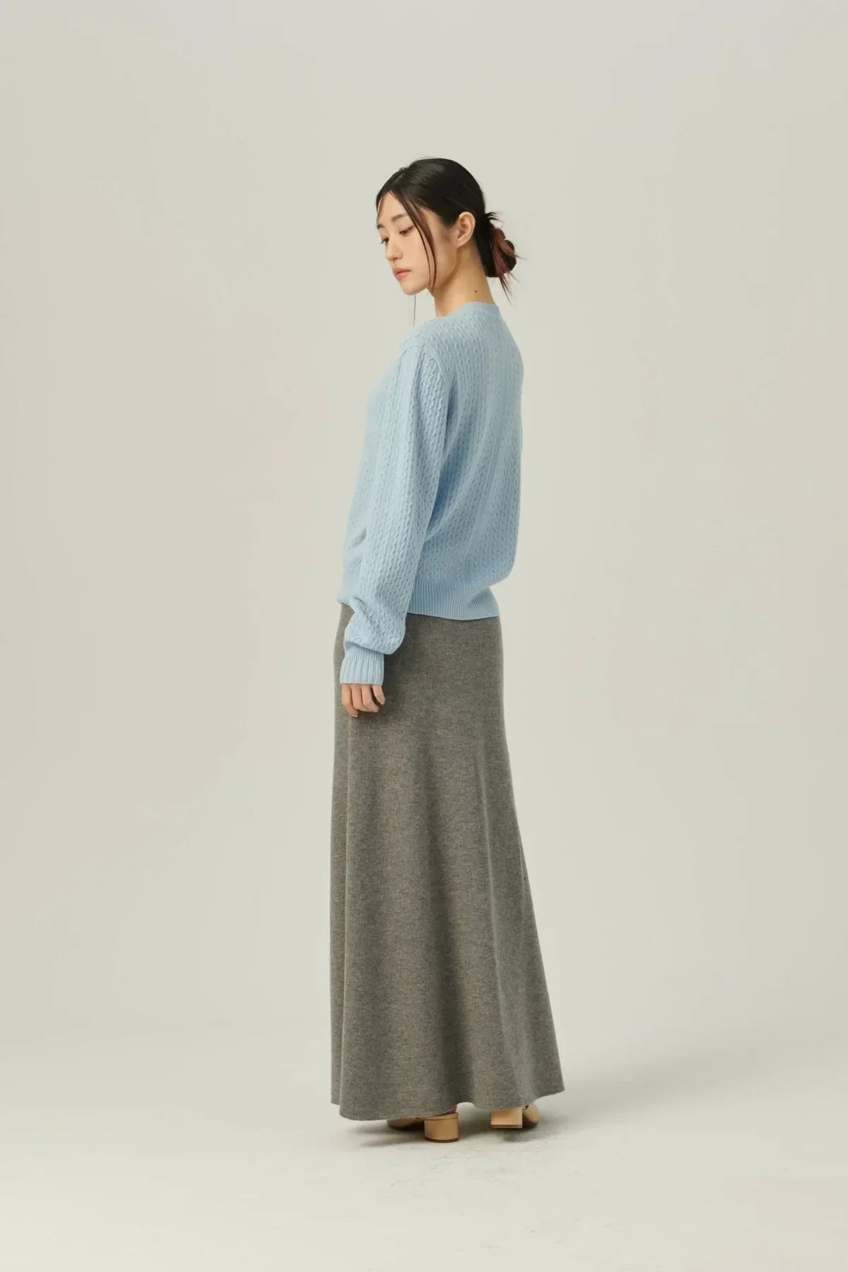 Woman wearing light blue knit sweater and long gray A-line knit skirt against plain background
