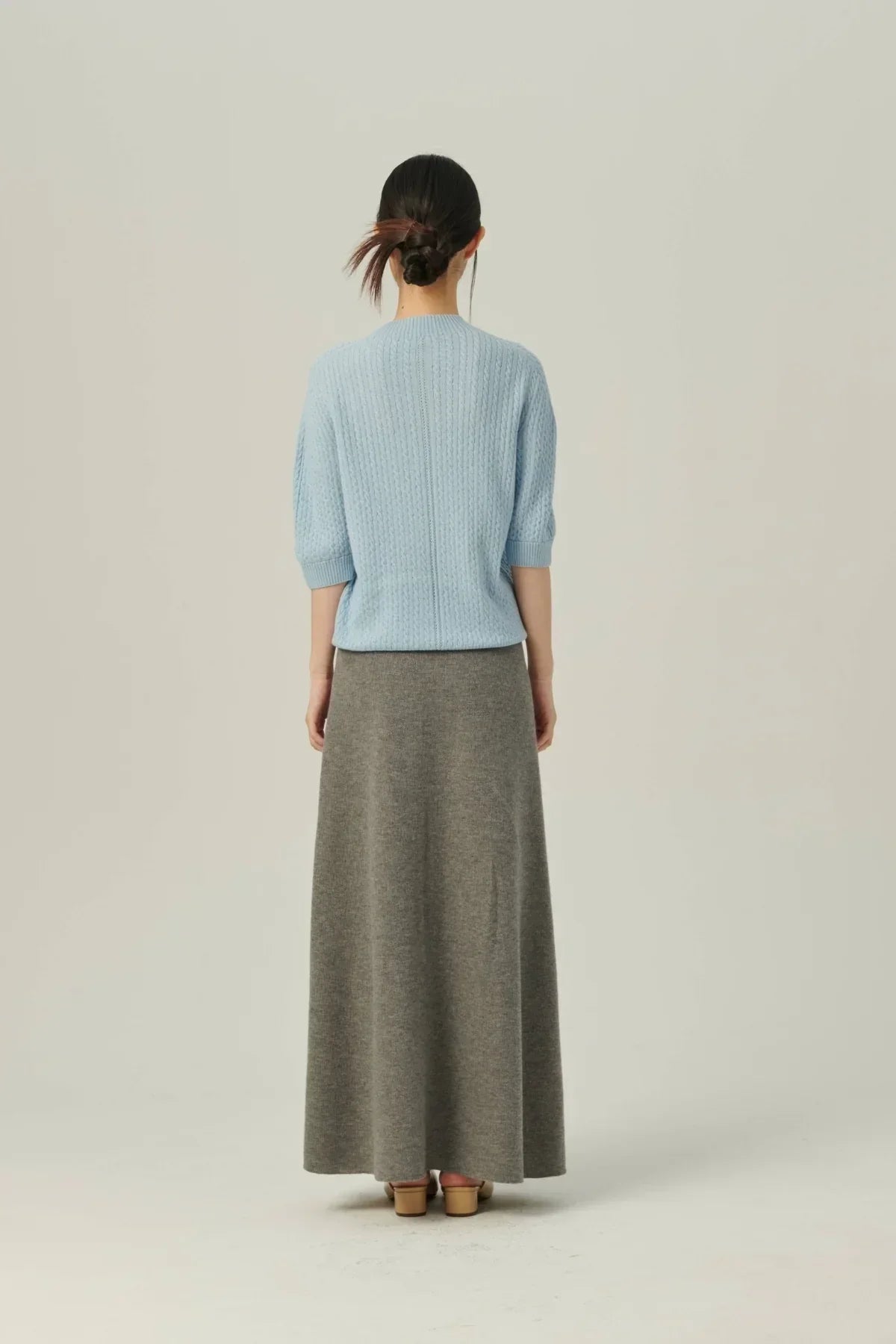 Woman wearing gray soft knit A-line skirt and light blue cable knit sweater facing away
