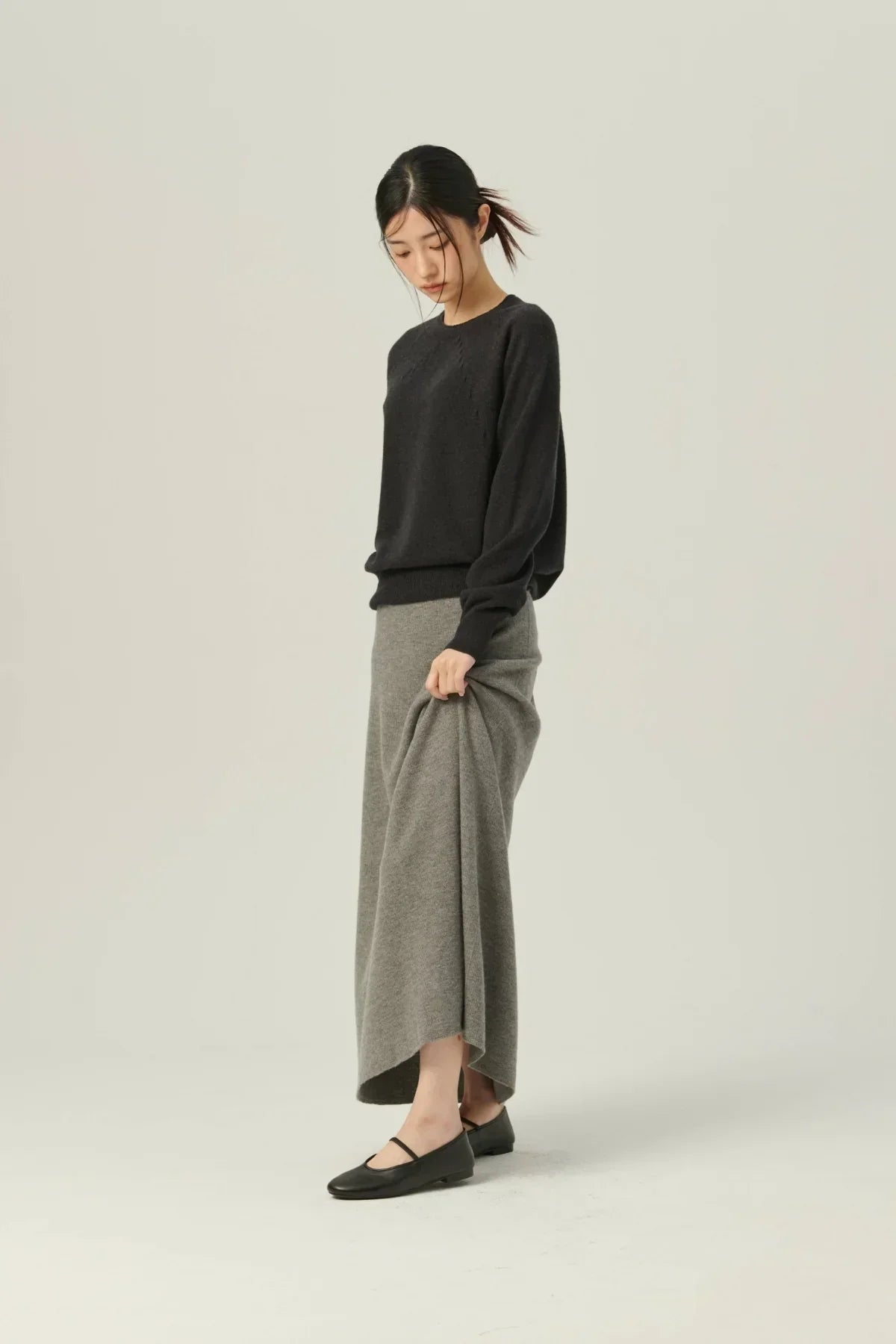 Young woman wearing black sweater and gray knit A-line skirt with black flats in studio