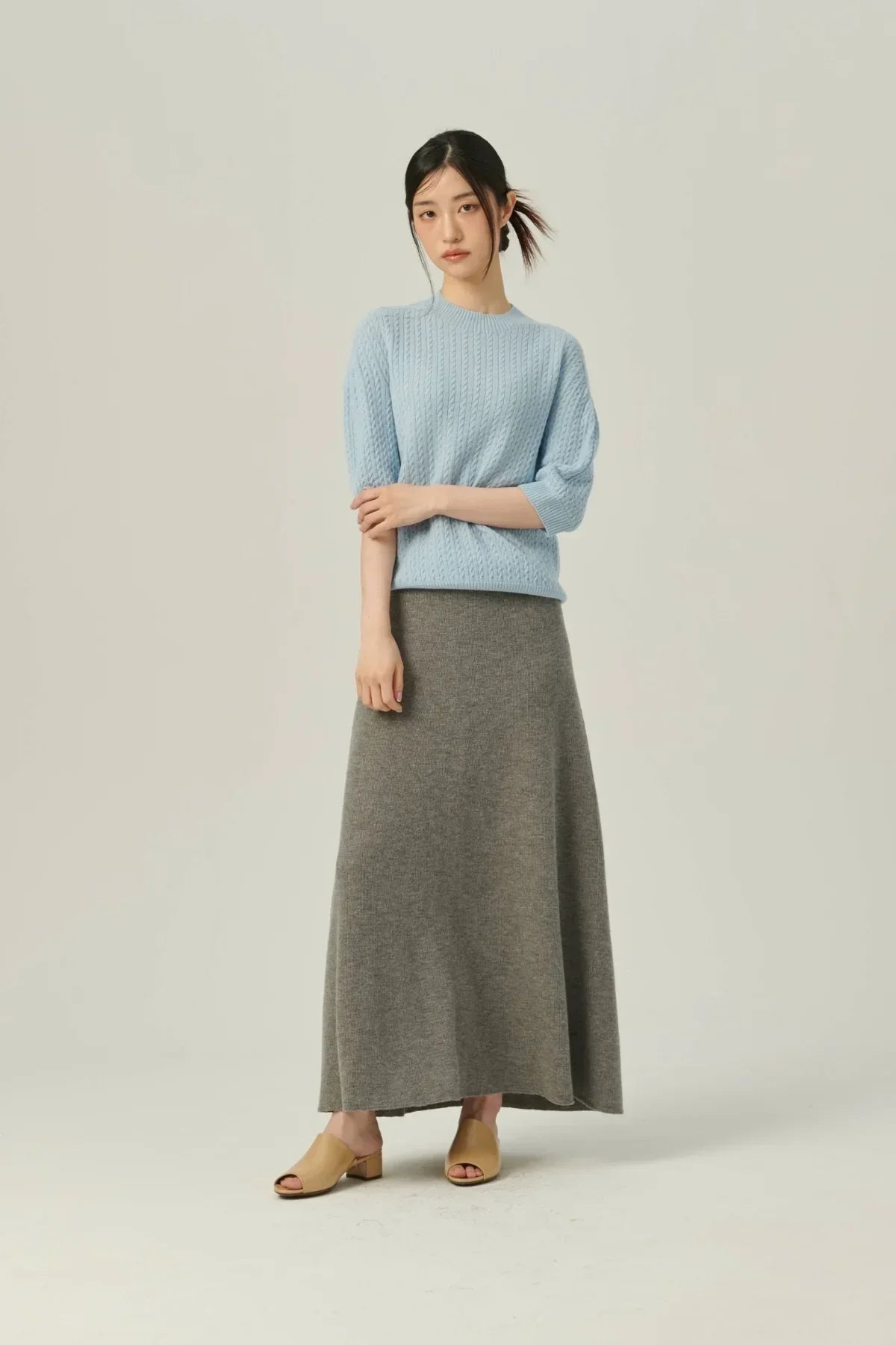 Woman wearing light blue cable knit sweater and gray soft A-line knit skirt with beige open-toe heels