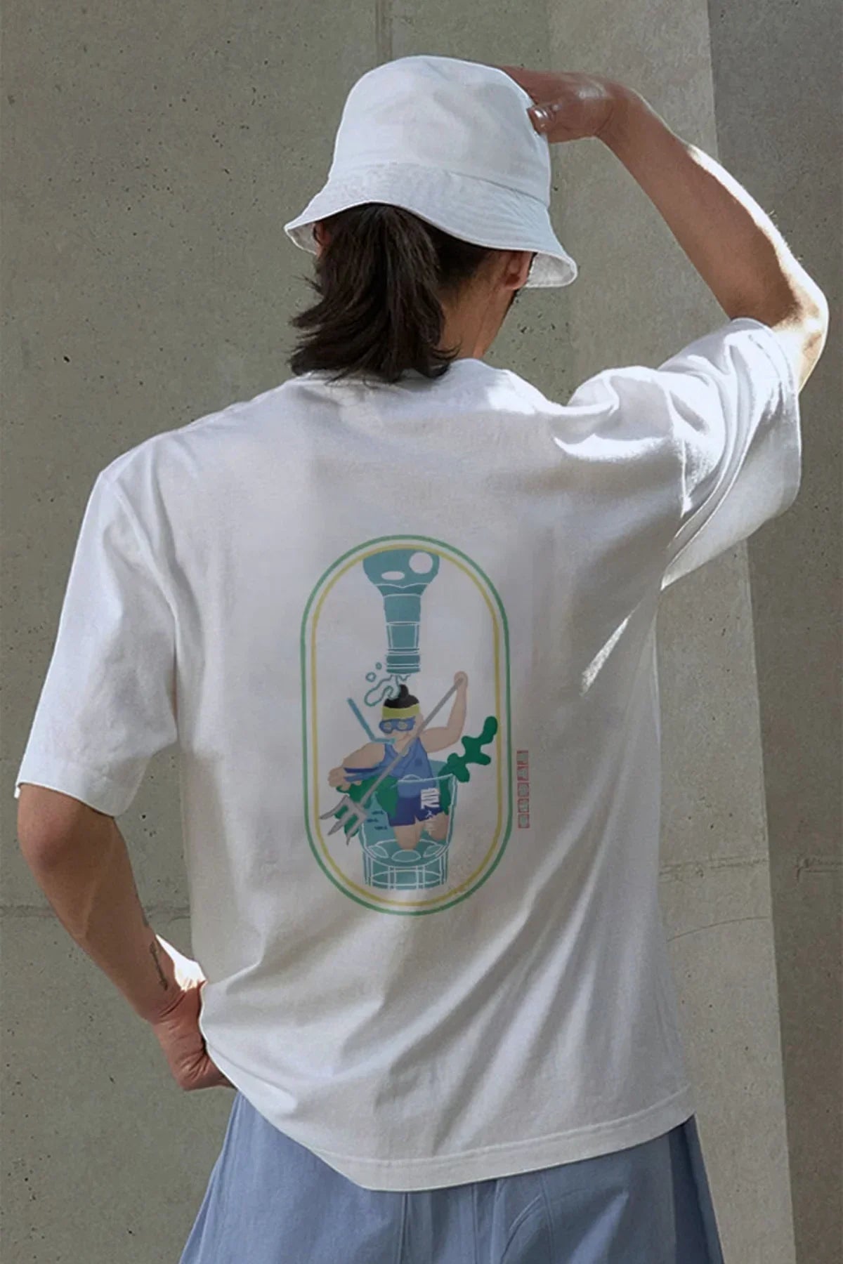 Person wearing white T-shirt with colorful underwater-themed graphic and white bucket hat in studio setting