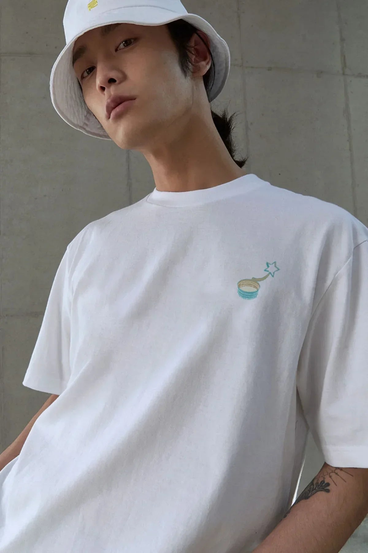 Young man wearing white graphic t-shirt with small star design and white bucket hat indoors