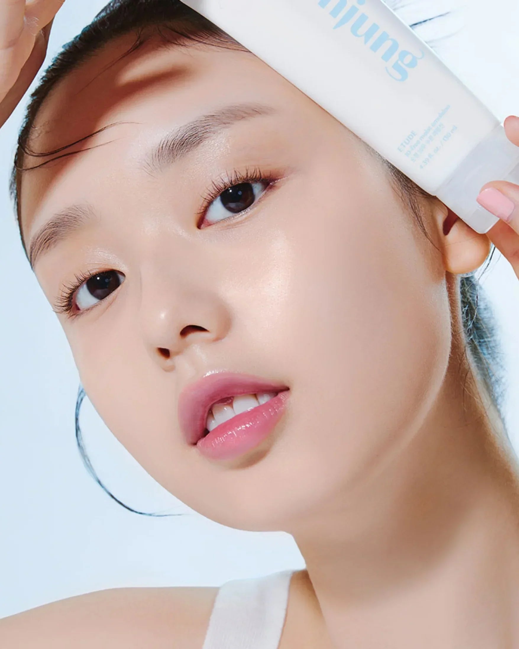 Close-up of model with clear glowing skin holding Soon Jung 10-Free Moist Emulsion skincare product