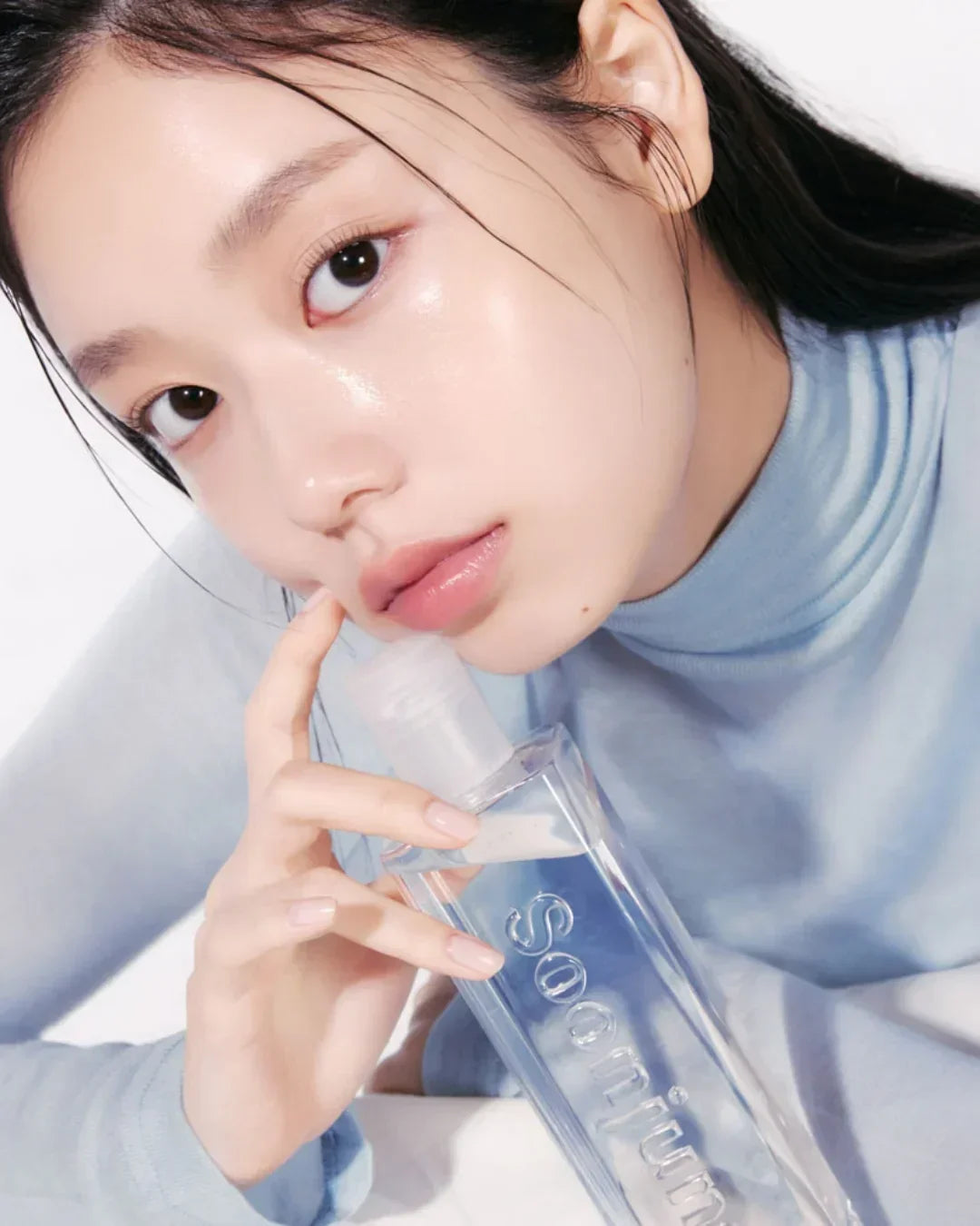 Close-up of woman with dewy skin holding Soon Jung PH 5.5 Relief Toner bottle, wearing light blue top