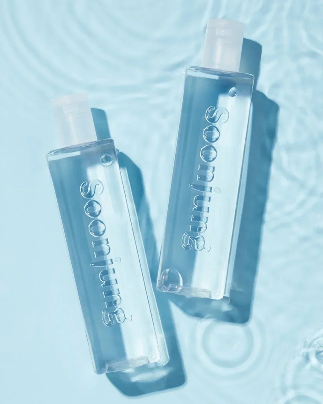Two clear Soomios skincare toner bottles on blue water surface with light ripples