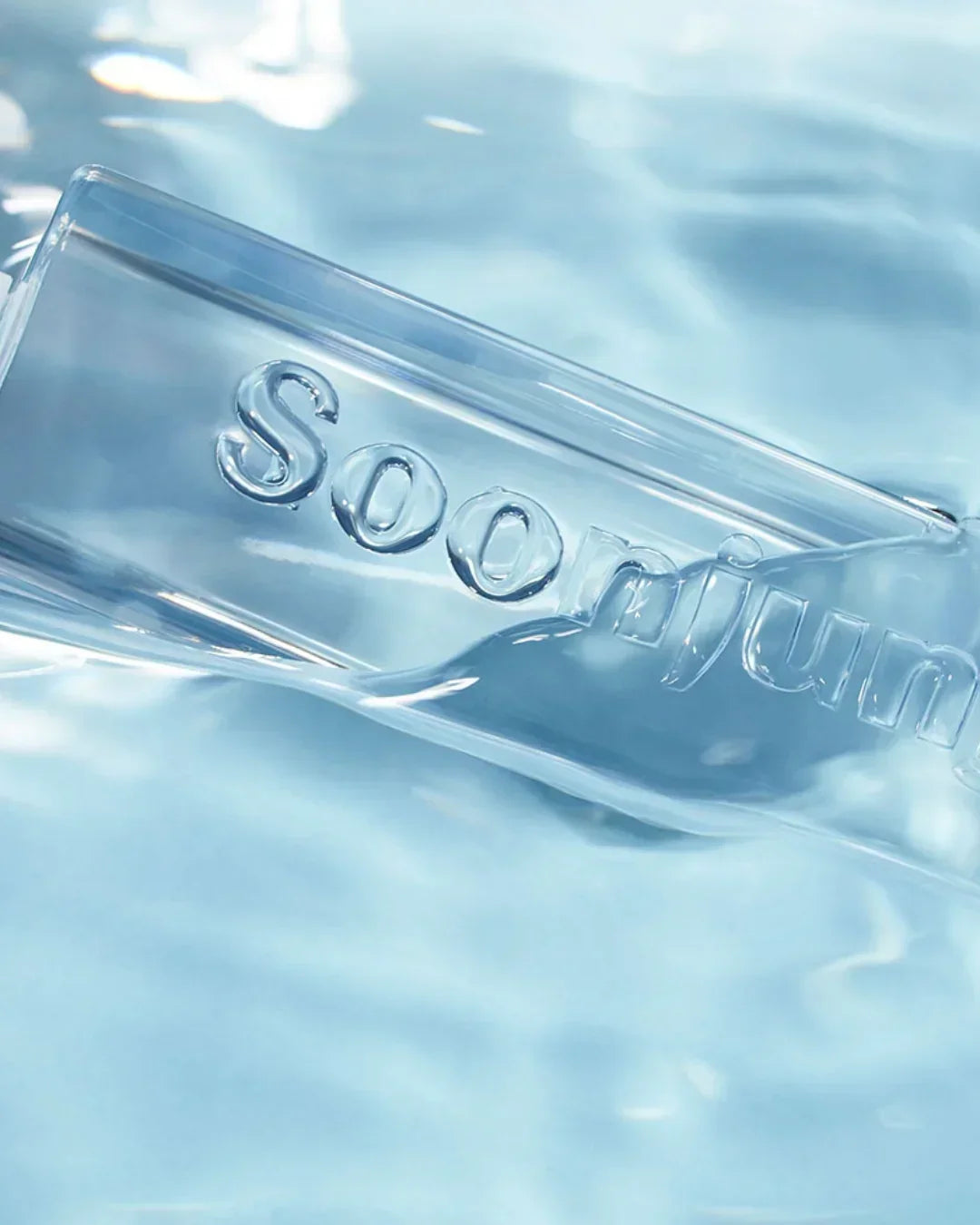 Clear Soon Jung bottle submerged in light blue water with embossed brand name
