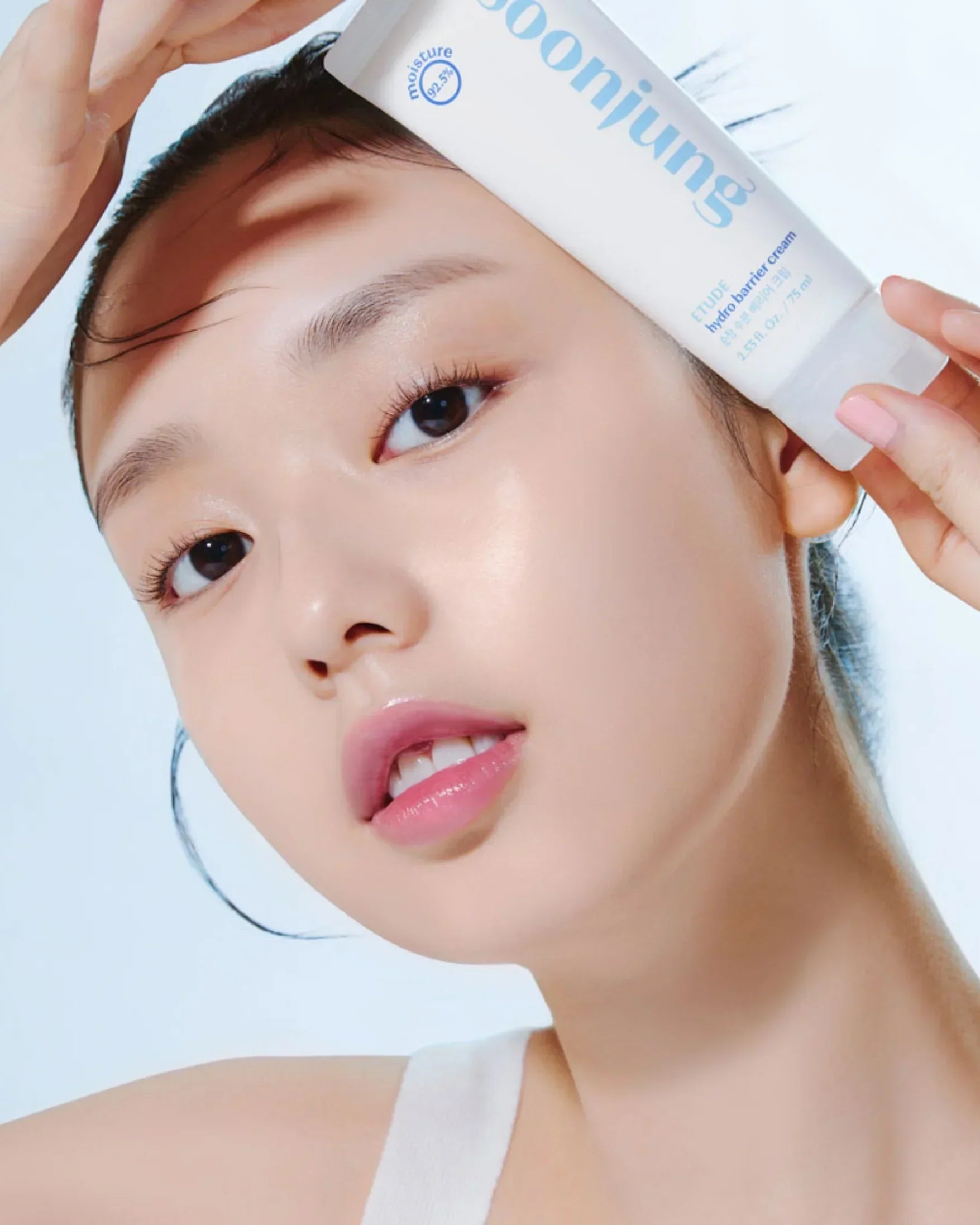 Close-up of a woman with clear skin holding Soonjung hydro barrier cream tube near her face