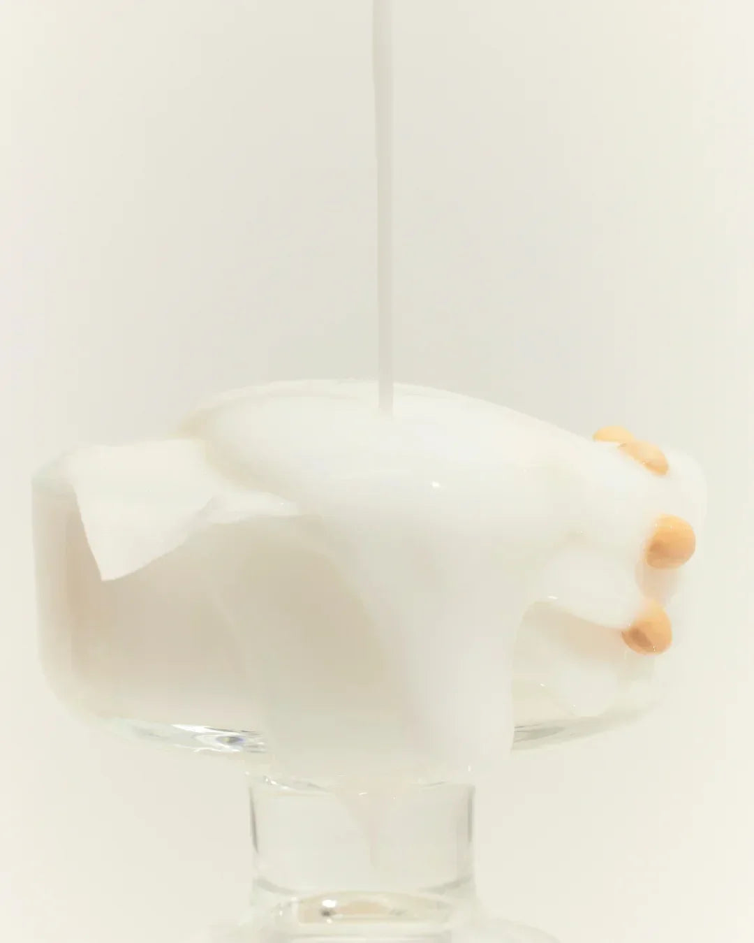 Glass bowl with white soybean milk pouring over soybeans and fabric in minimalistic setting
