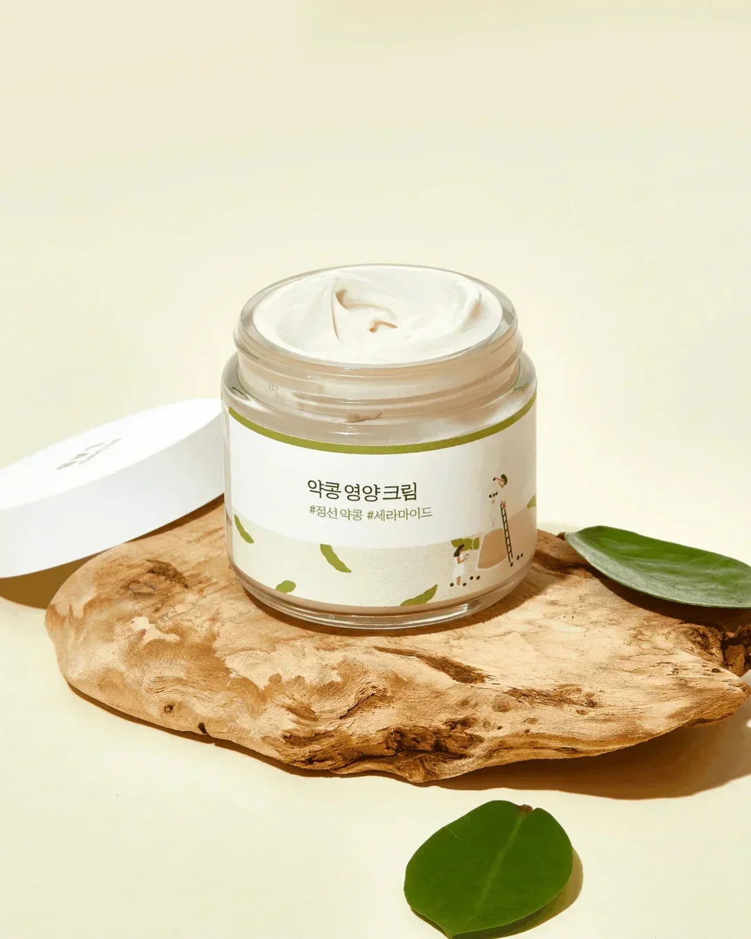 Open jar of soybean nourishing cream on wooden board with green leaves in soft beige setting