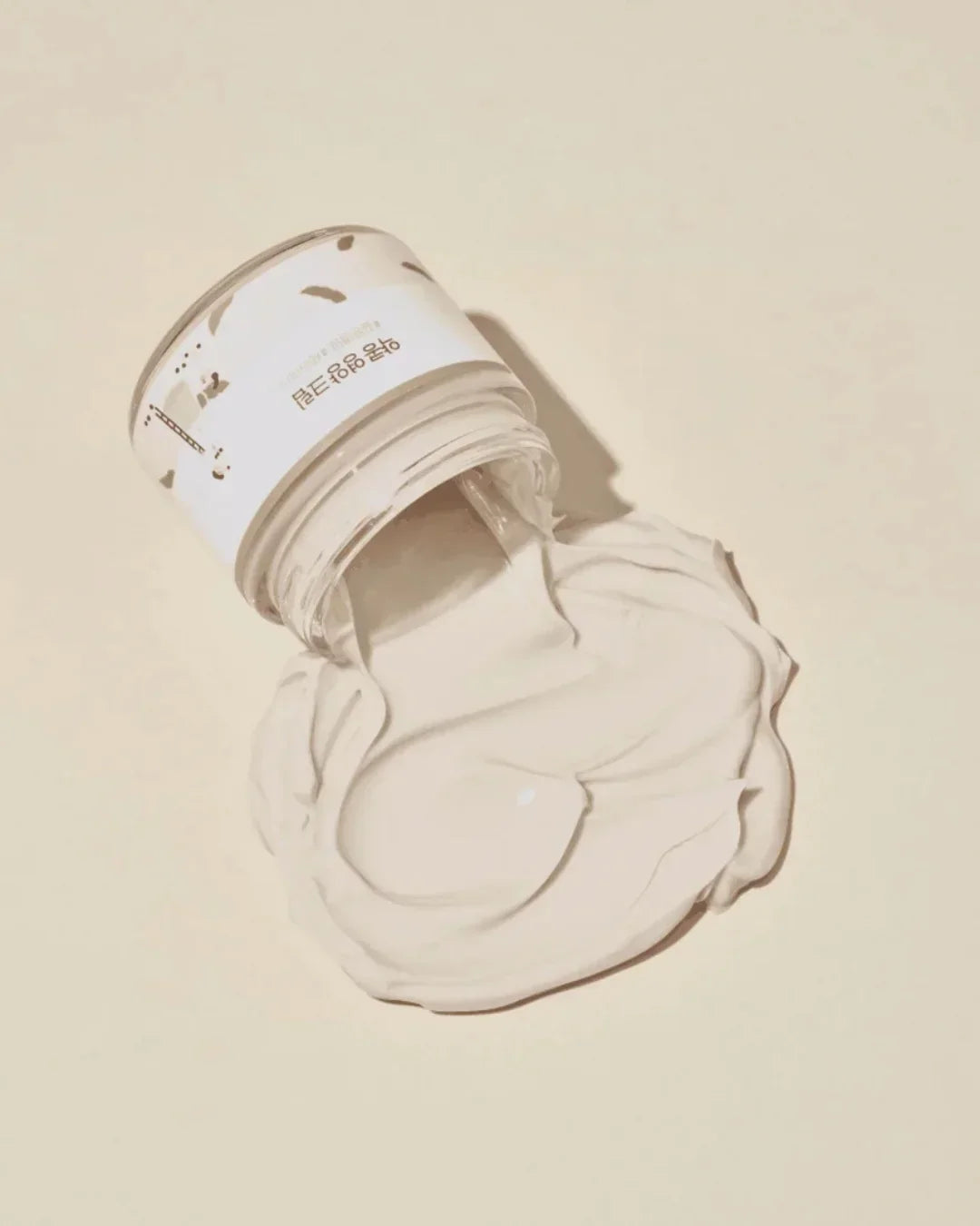 Open jar of soybean nourishing cream with smooth white texture spread on beige surface