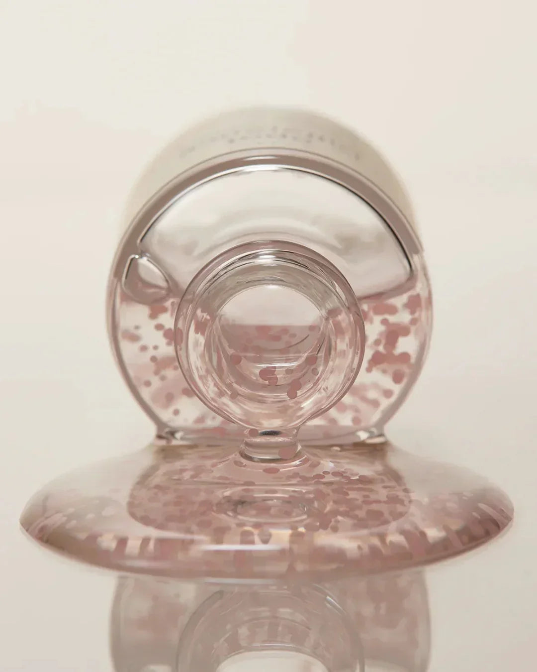 Close-up of clear spot treatment gel with pink beads spread on reflective surface