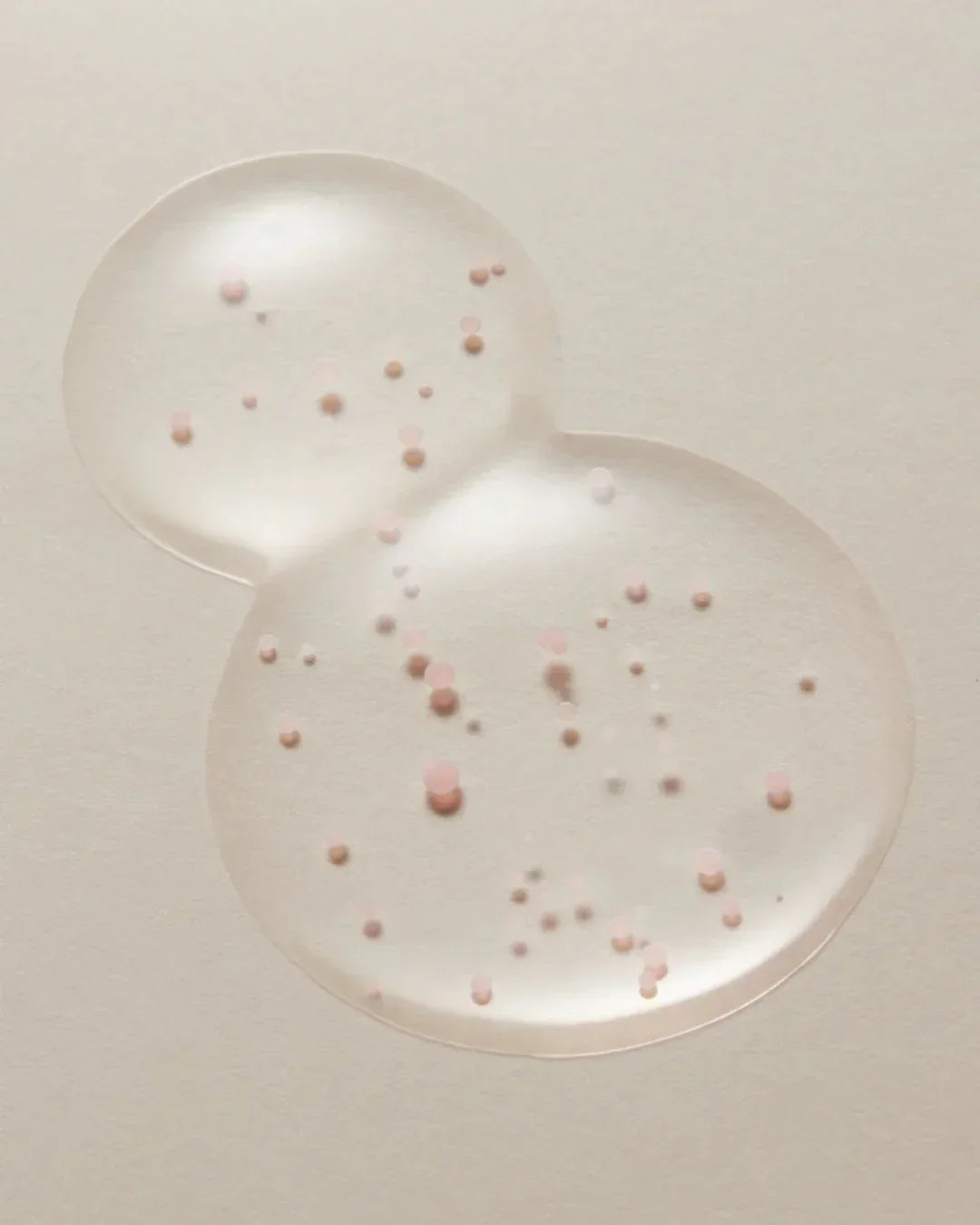 Clear blemish treatment gel texture with pink exfoliating beads on beige background