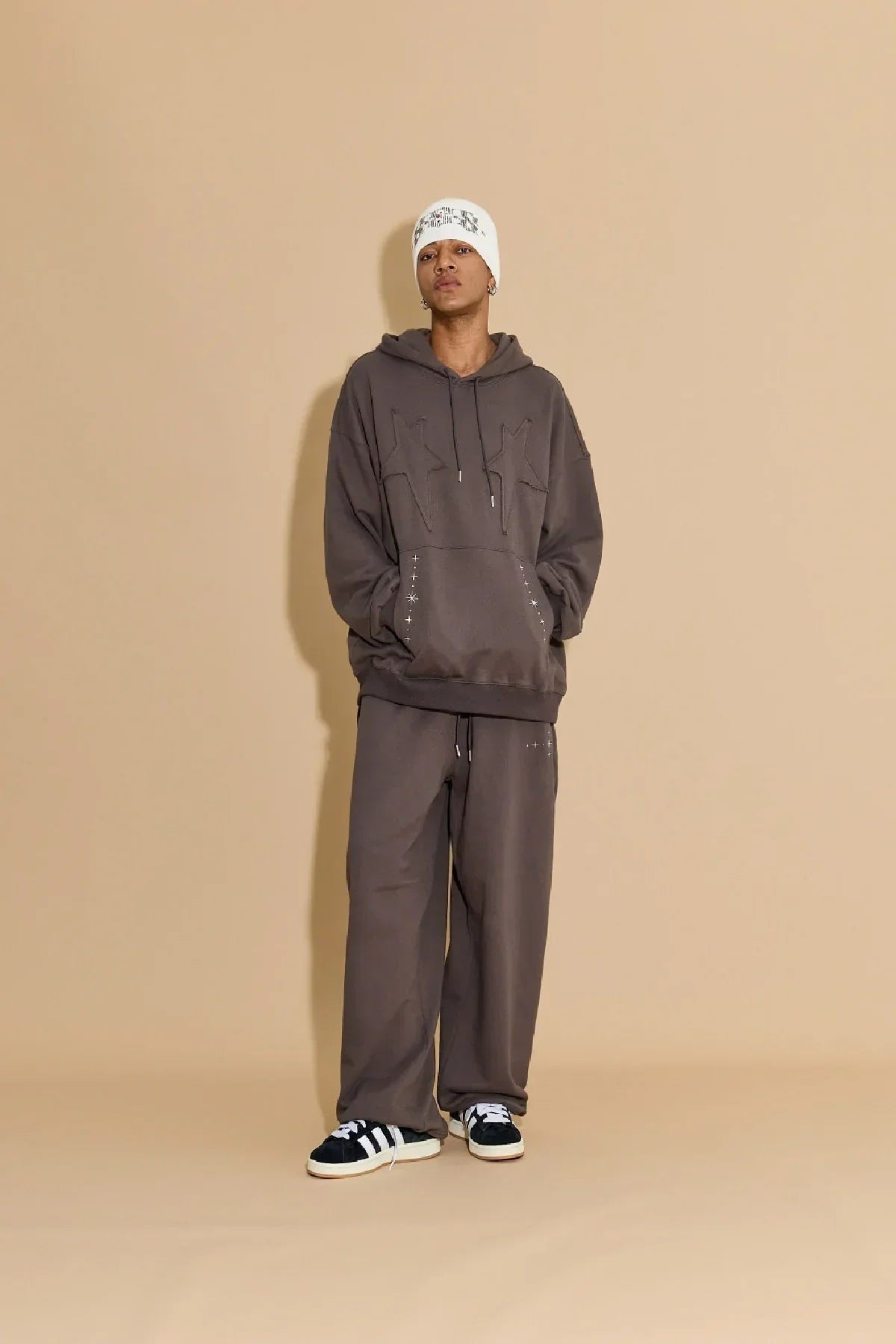 Model wearing charcoal star applique embroidery hoodie and sweatpants with white beanie and black sneakers
