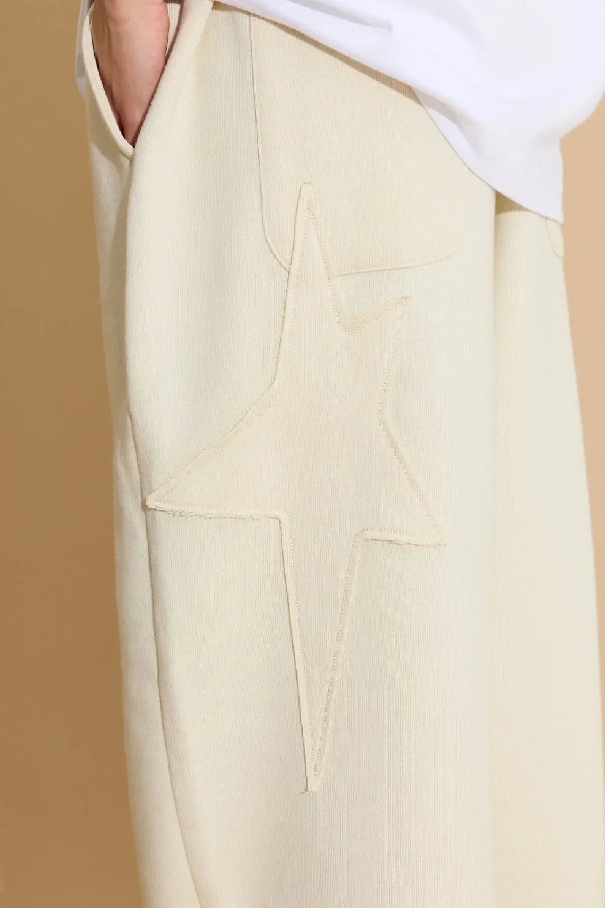 Close-up of ivory sweatpants with large star applique embroidery detail and side pocket