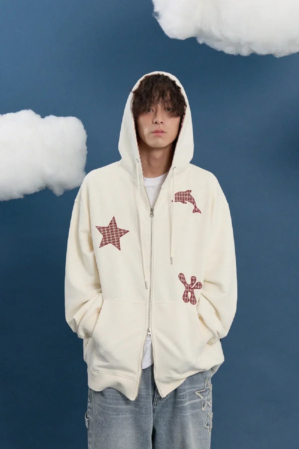 Man wearing ivory zip-up hoodie with red star, dolphin, and abstract check patches, Korean fashion style, blue background with clouds, Malkn lifestyle platform.