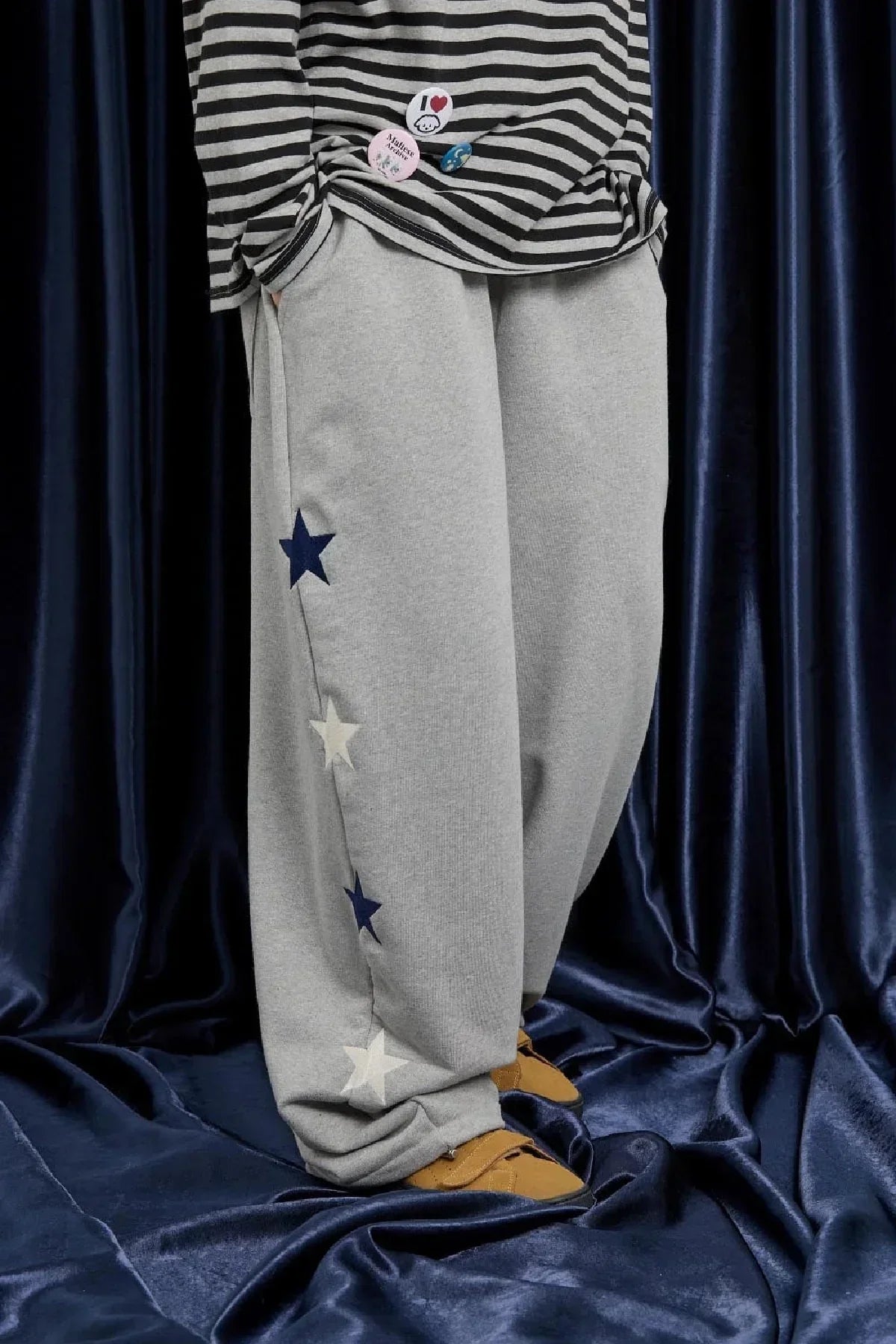 Close-up of grey sweatpants with blue and white star designs on side, paired with striped shirt and yellow shoes