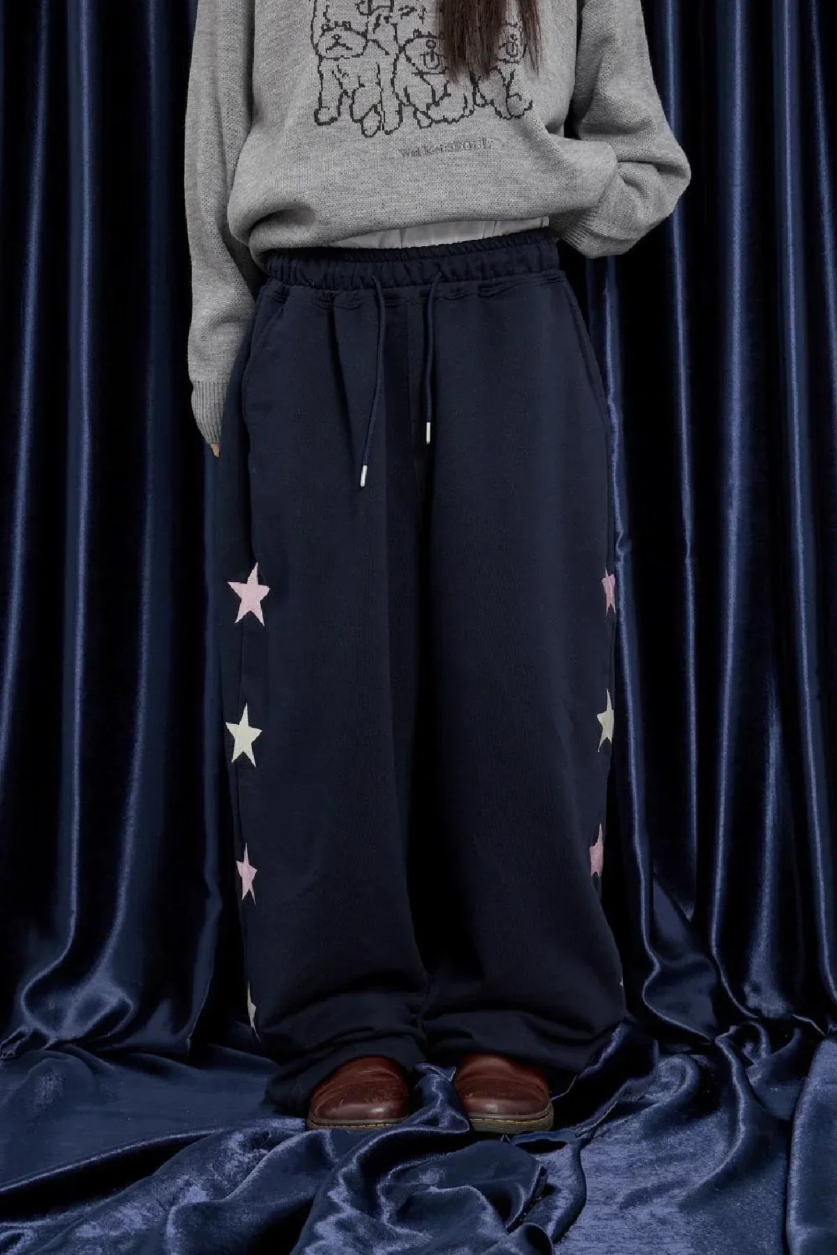 Navy blue sweatpants with pink and white star prints on sides, worn with gray sweater and brown shoes
