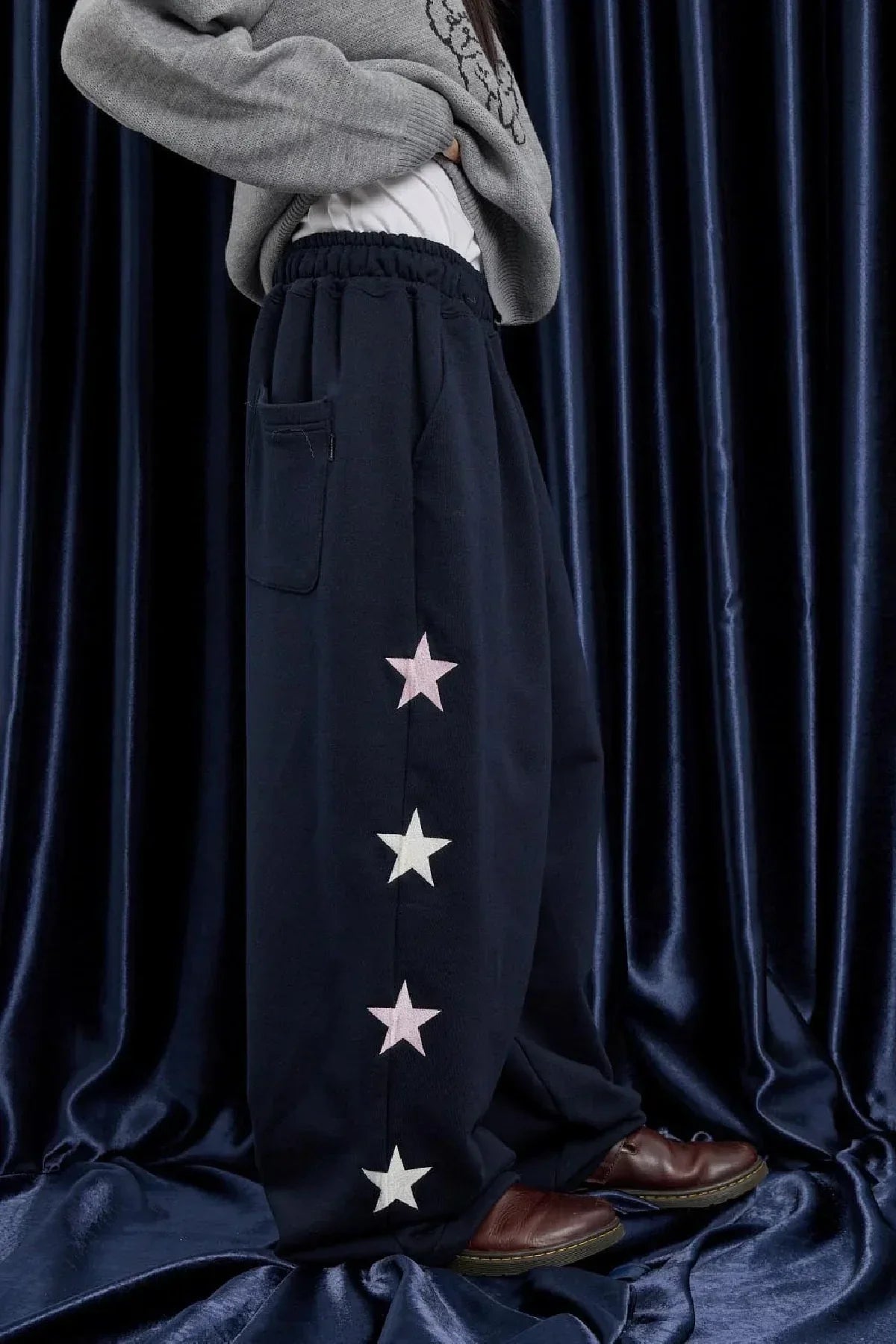Close-up of navy star sweatpants with elastic waist and pocket, worn with brown shoes and gray sweater